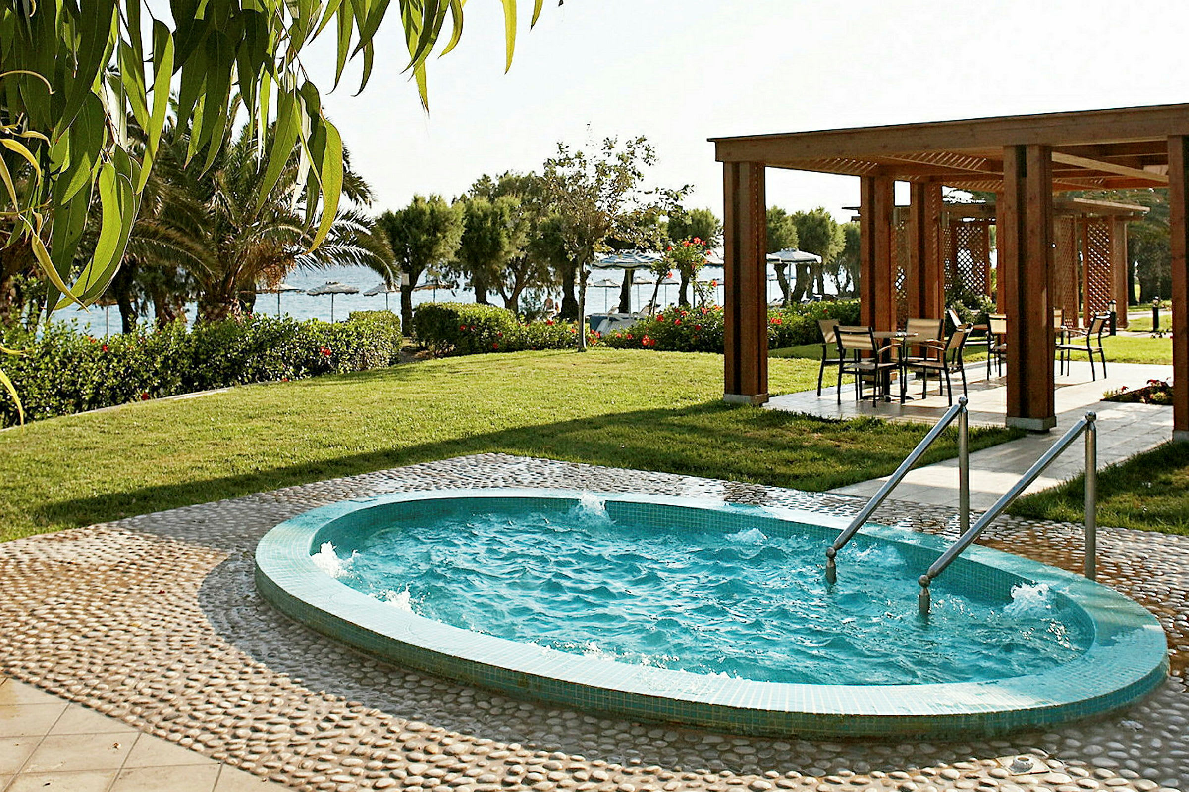 Billede af en lille udendørs pool med gelænder, omgivet af frodig have og en pergola område med siddepladser. (AI-genereret tekst)
