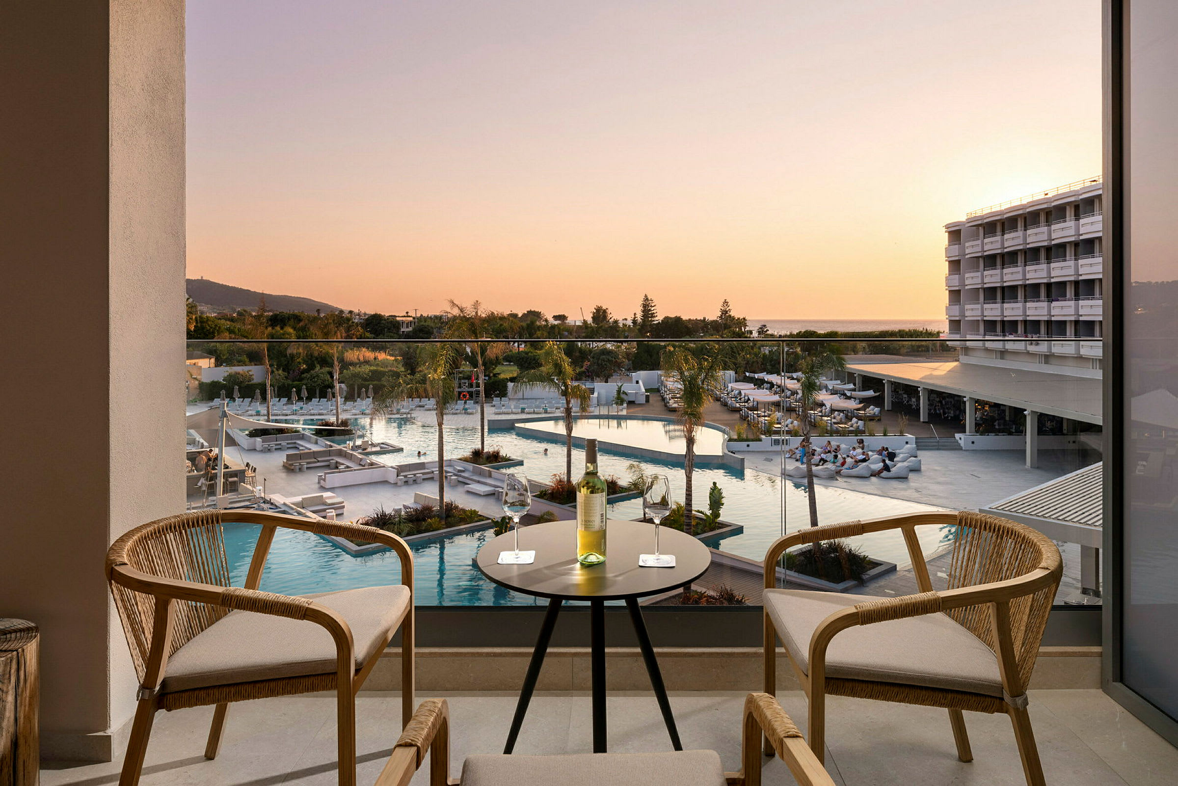 Udendørsområde med bord og stole, udsigt over poolområde og hotelbygning ved solnedgang. (AI-genereret tekst)
