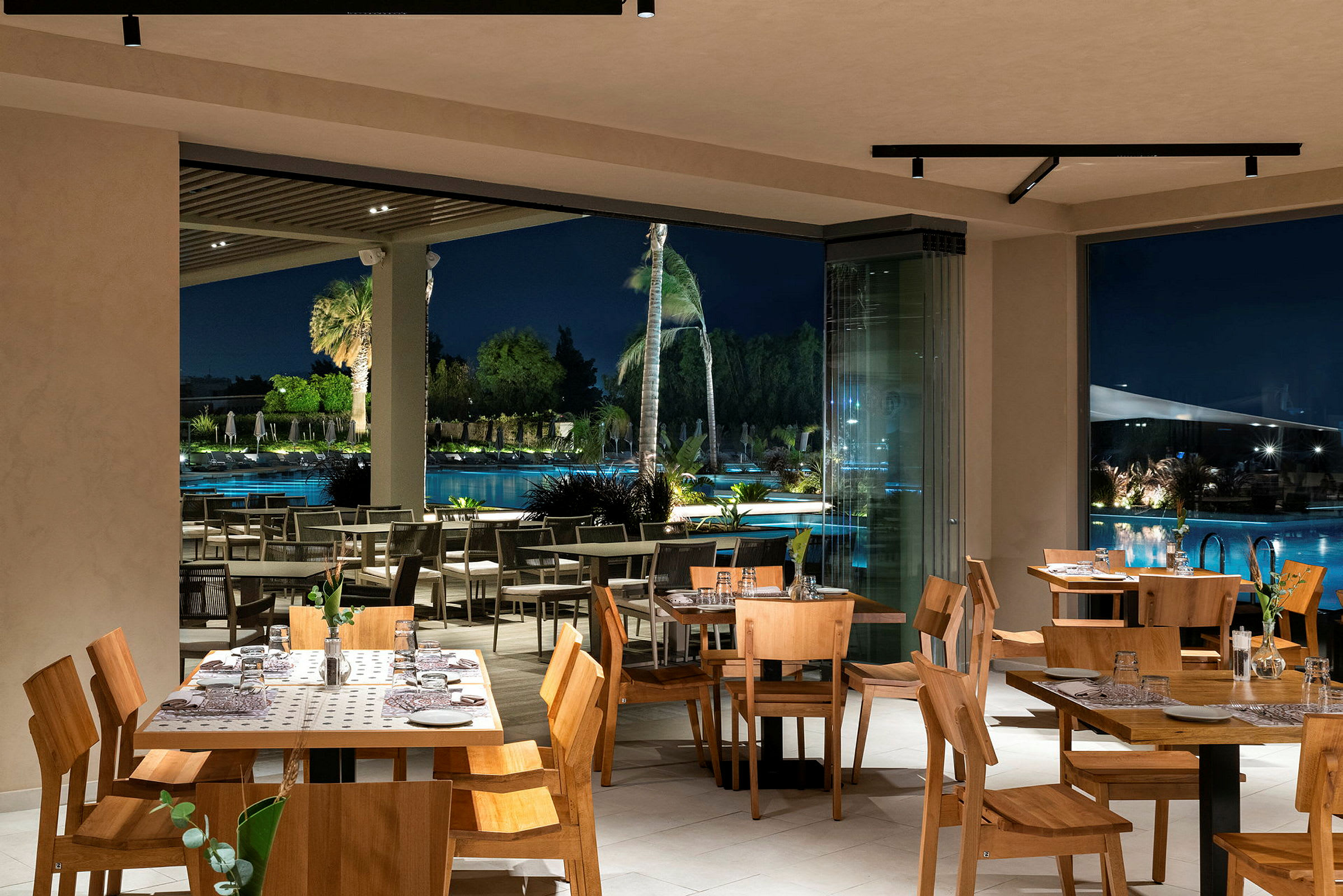 Restaurantinteriør med træborde og stole, udsigt over poolområdet om natten. (AI-genereret tekst)