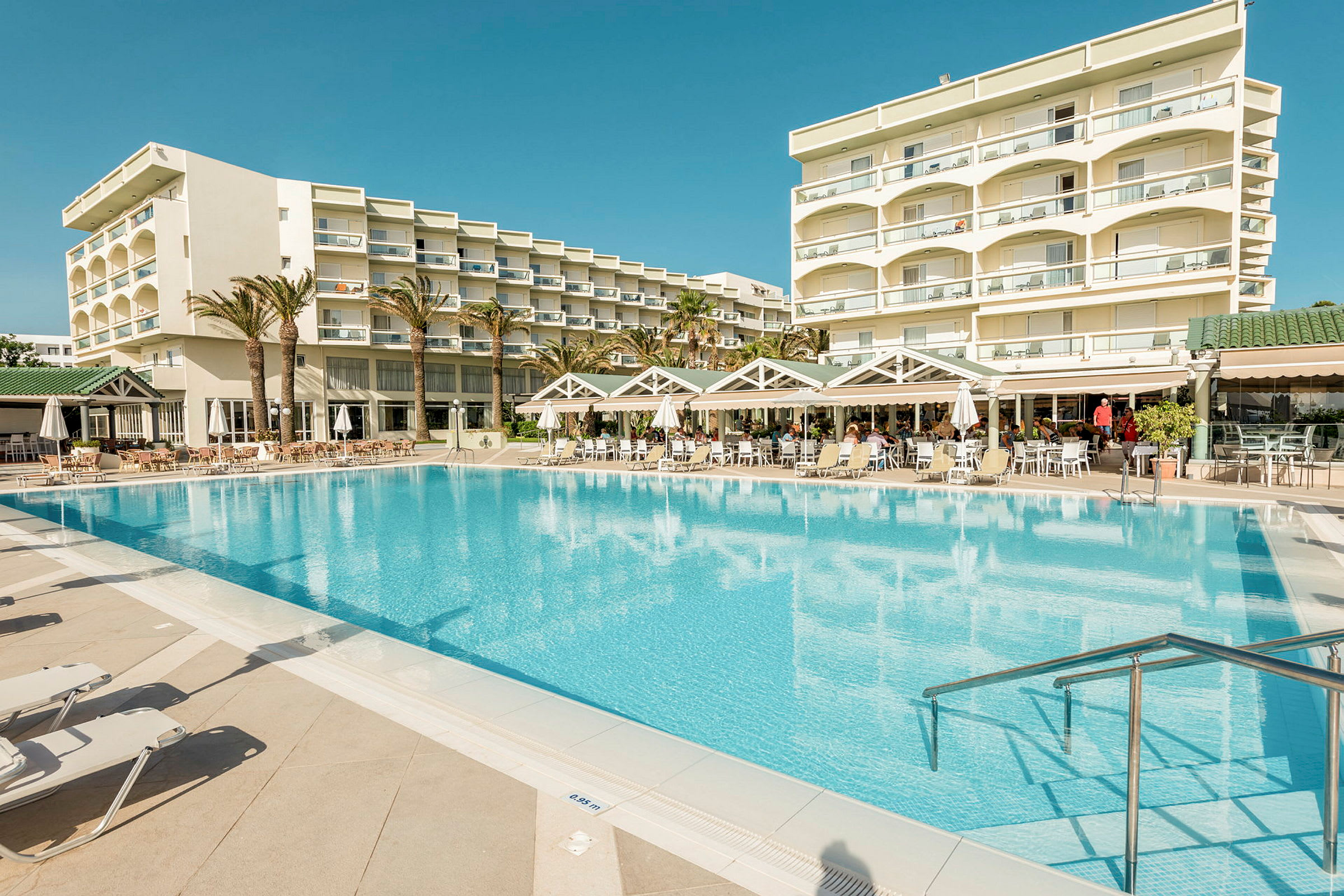 Udendørs swimmingpool med liggestole og en hotelbygning i baggrunden. (AI-genereret tekst)