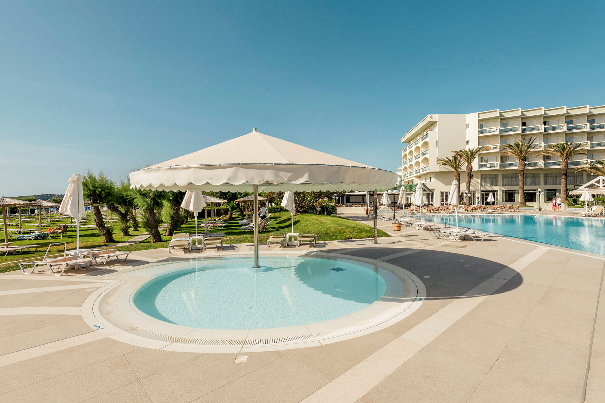 Udendørs poolområde med solsenge, parasoller og hotelbygning i baggrunden. (AI-genereret tekst)