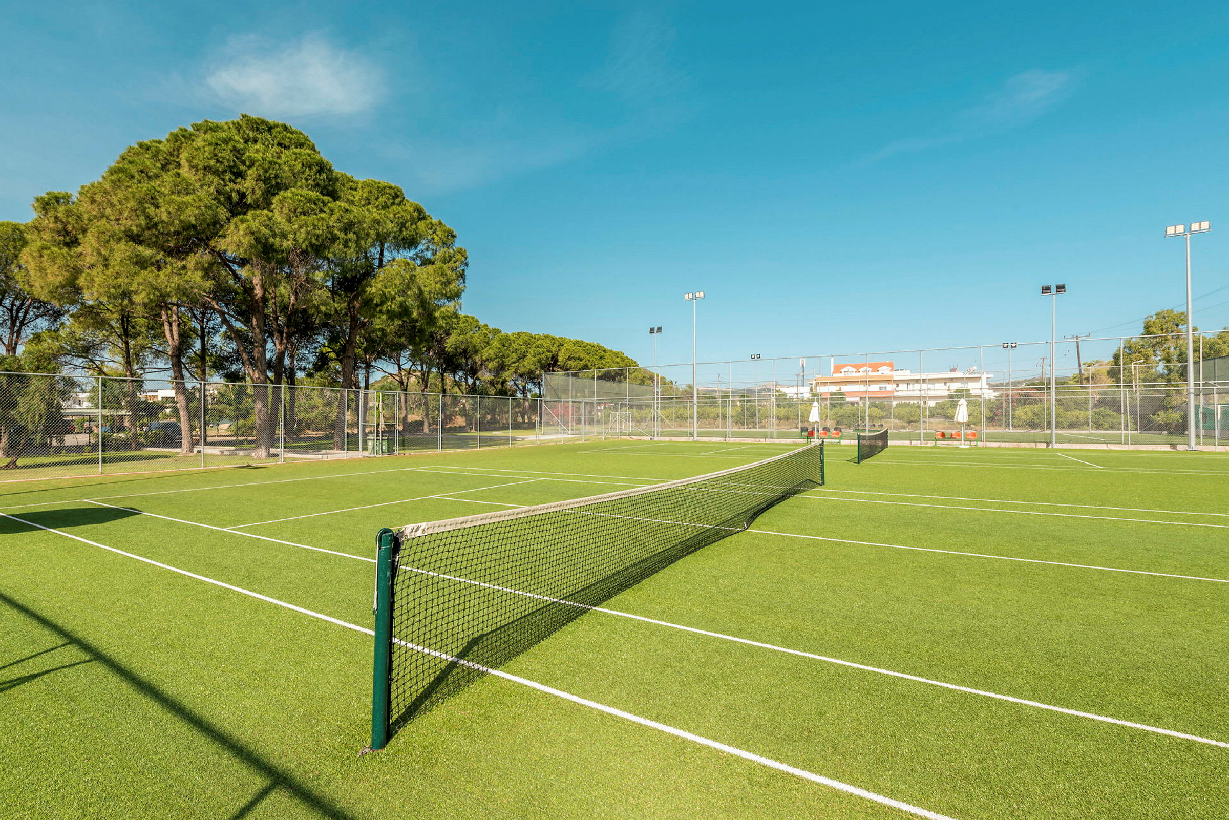 En grøn tennisbane med net og omkringliggende hegn. (AI-genereret tekst)