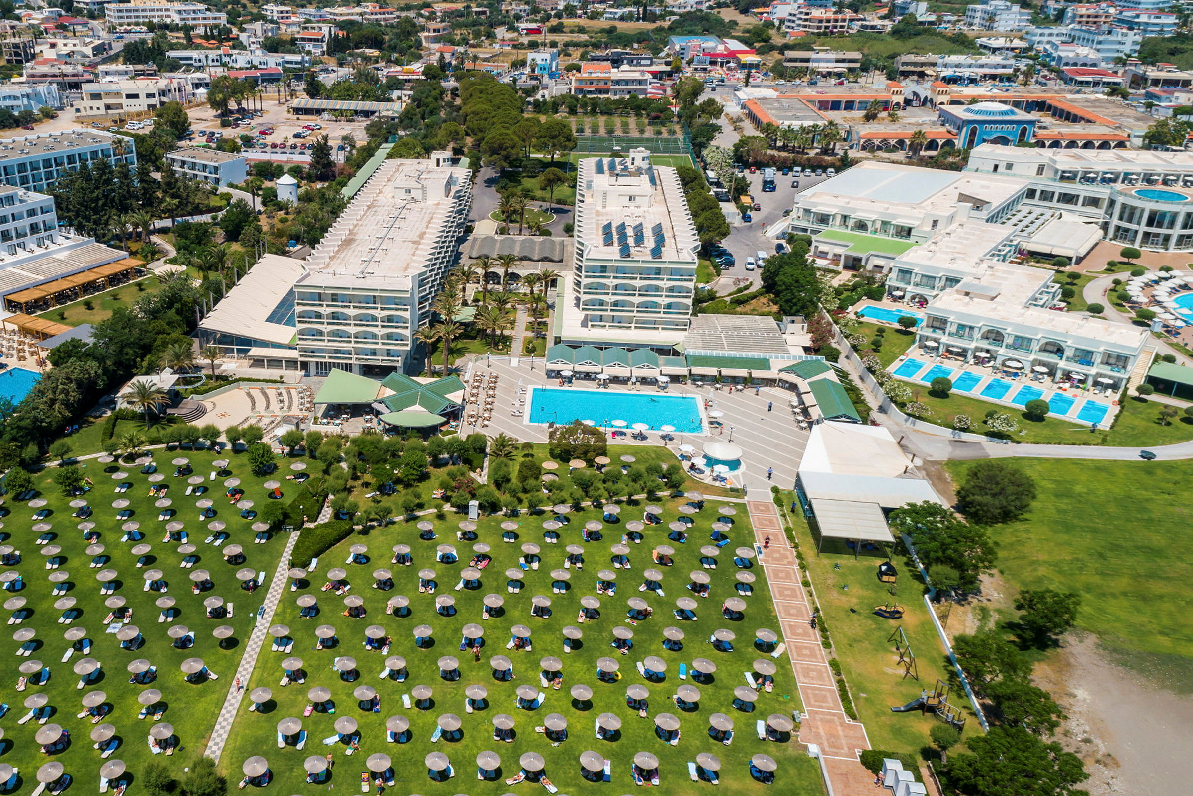 Luftfoto af hotelkompleks med pools, bygninger og grønne områder. (AI-genereret tekst)
