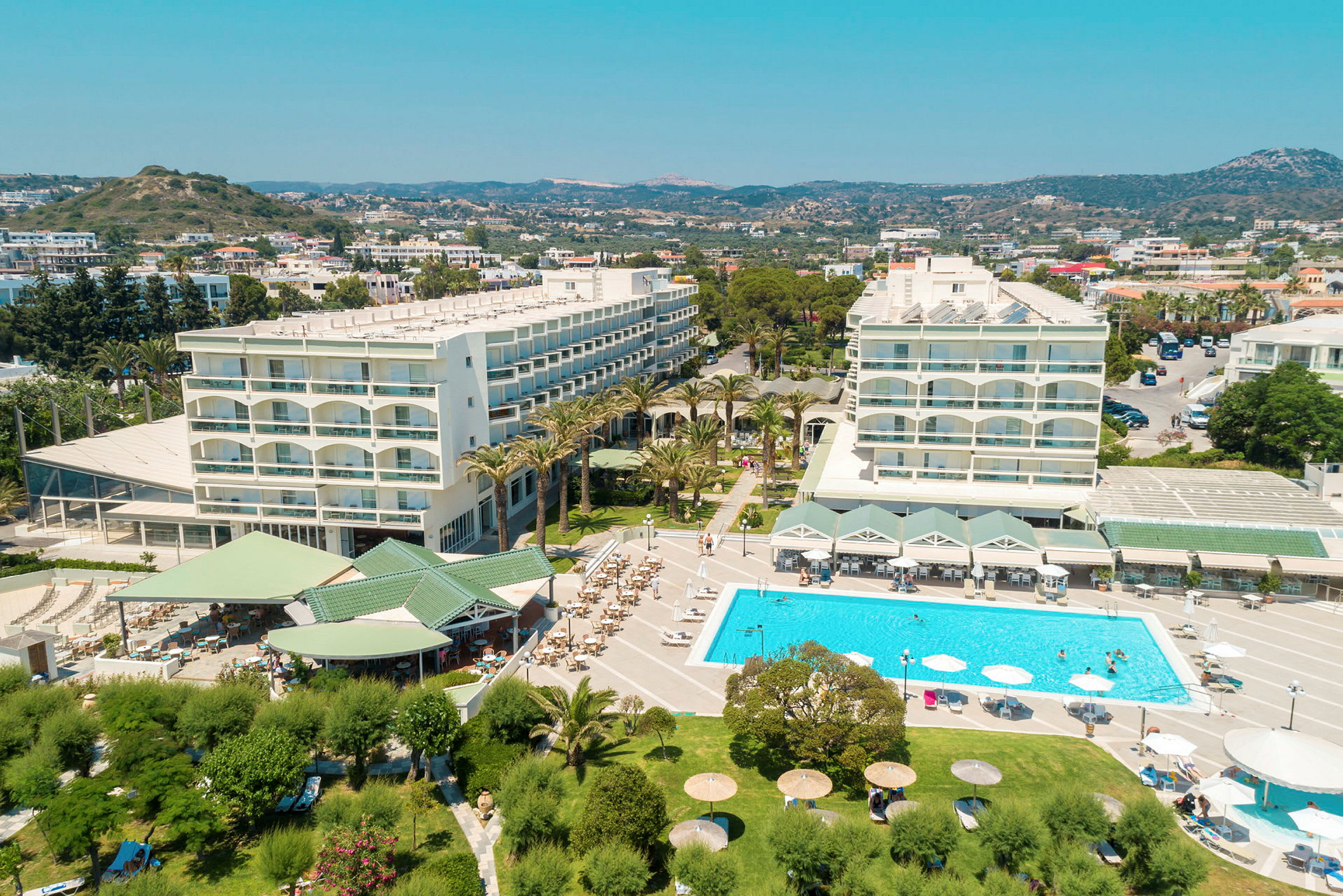 Luftfoto af et hotelområde med pool, grøn have og bygninger. (AI-genereret tekst)