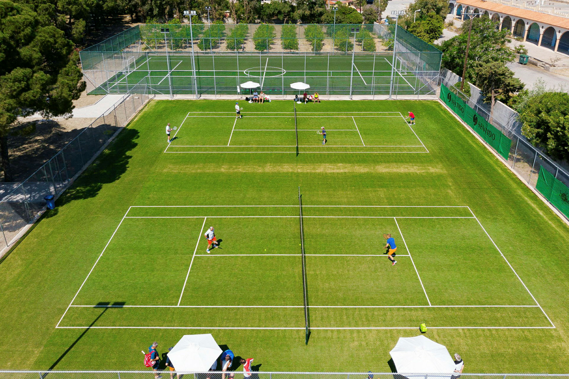 Luftfoto af en tennisbane med spillere og omkringliggende træer. (AI-genereret tekst)