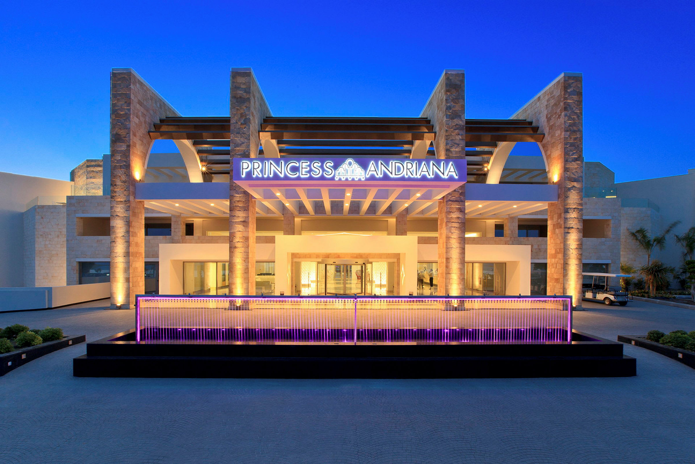 Hotellets indgang med skiltet "Princess Andriana" og moderne arkitektur. (AI-genereret tekst)