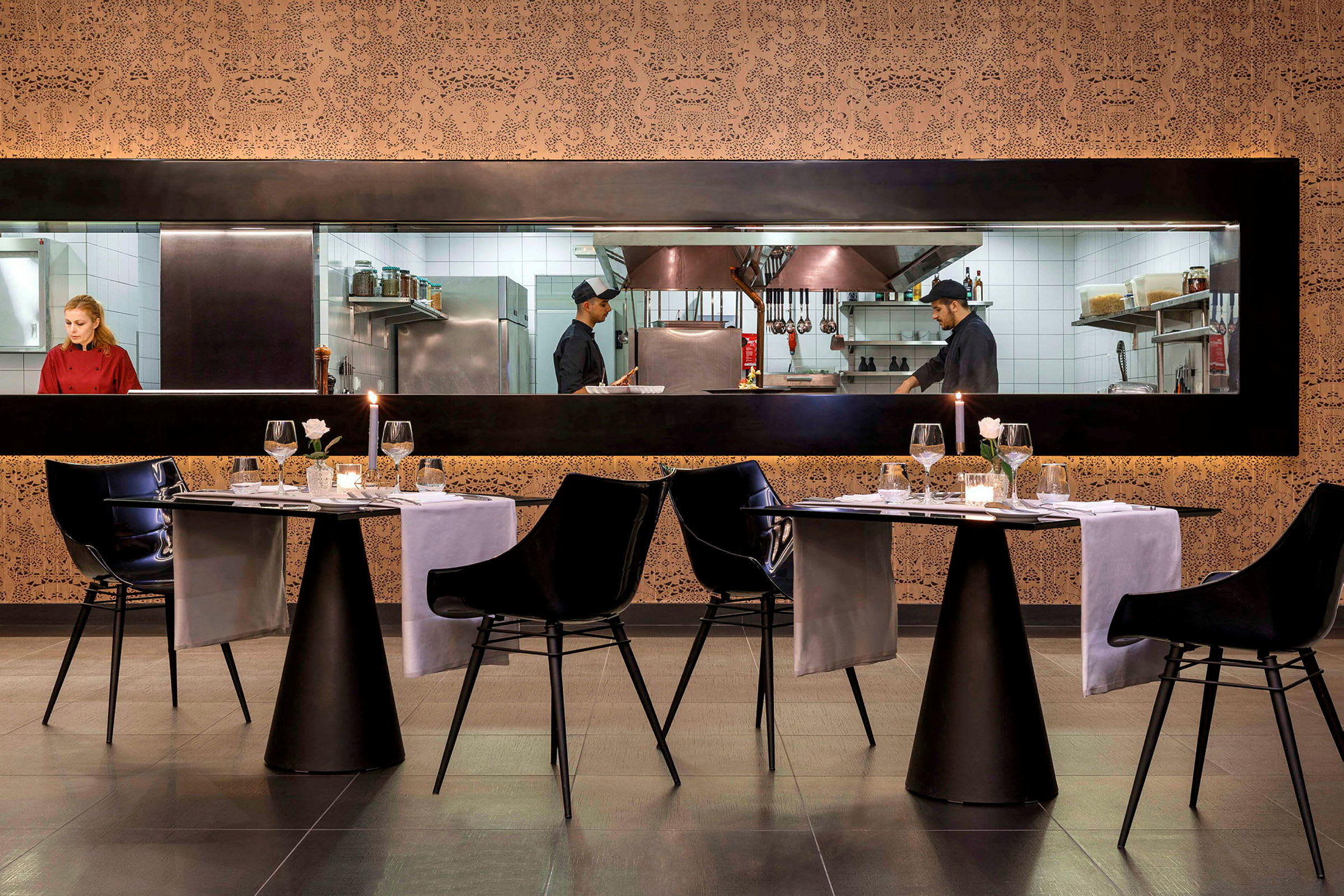 Billede af en restaurant med oplyste bordanretninger og synligt køkken gennem en glasrude. (AI-genereret tekst)
