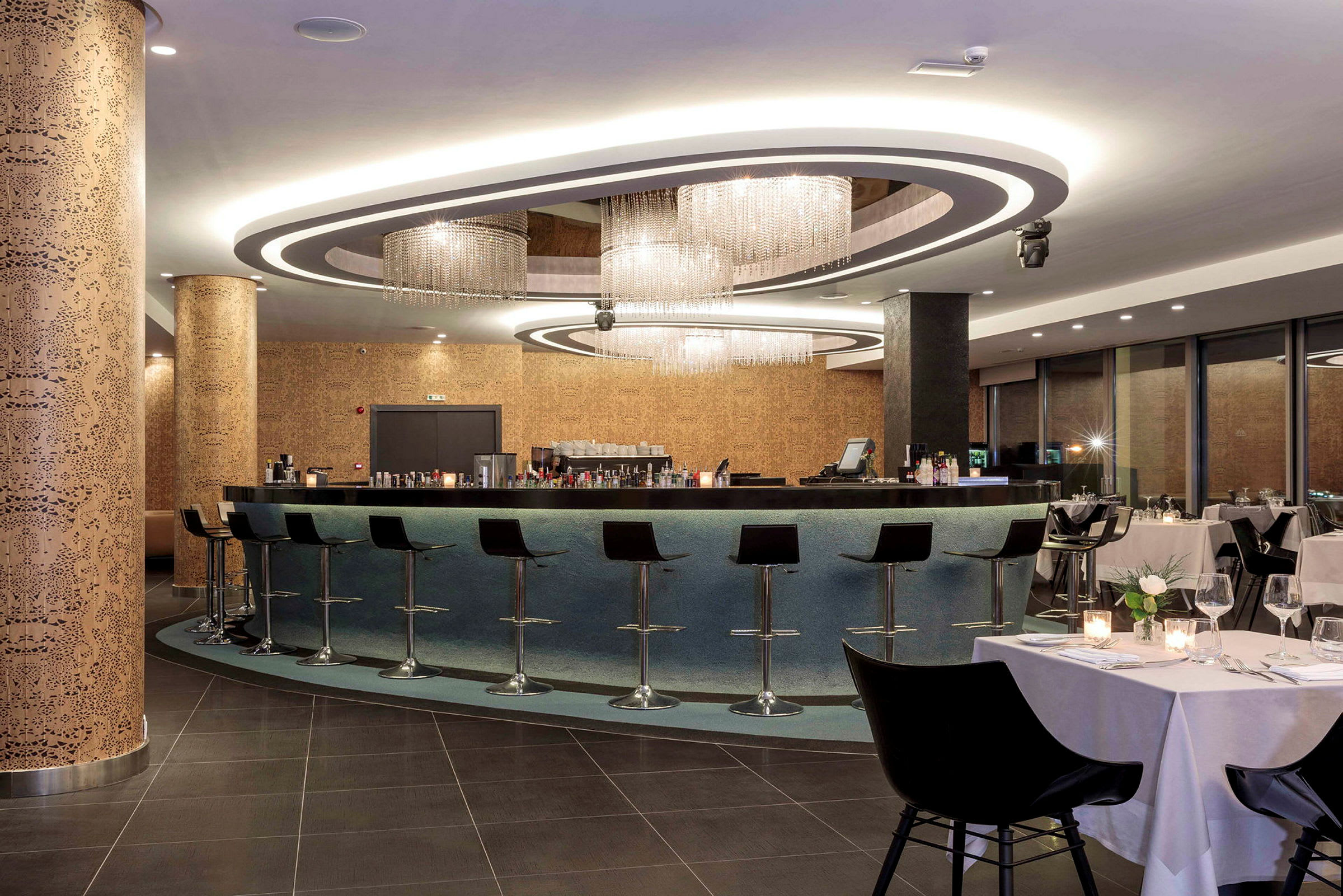 En moderne bar med høje stole og elegant lysdesign, omgivet af en restaurant med dækkede borde. (AI-genereret tekst)
