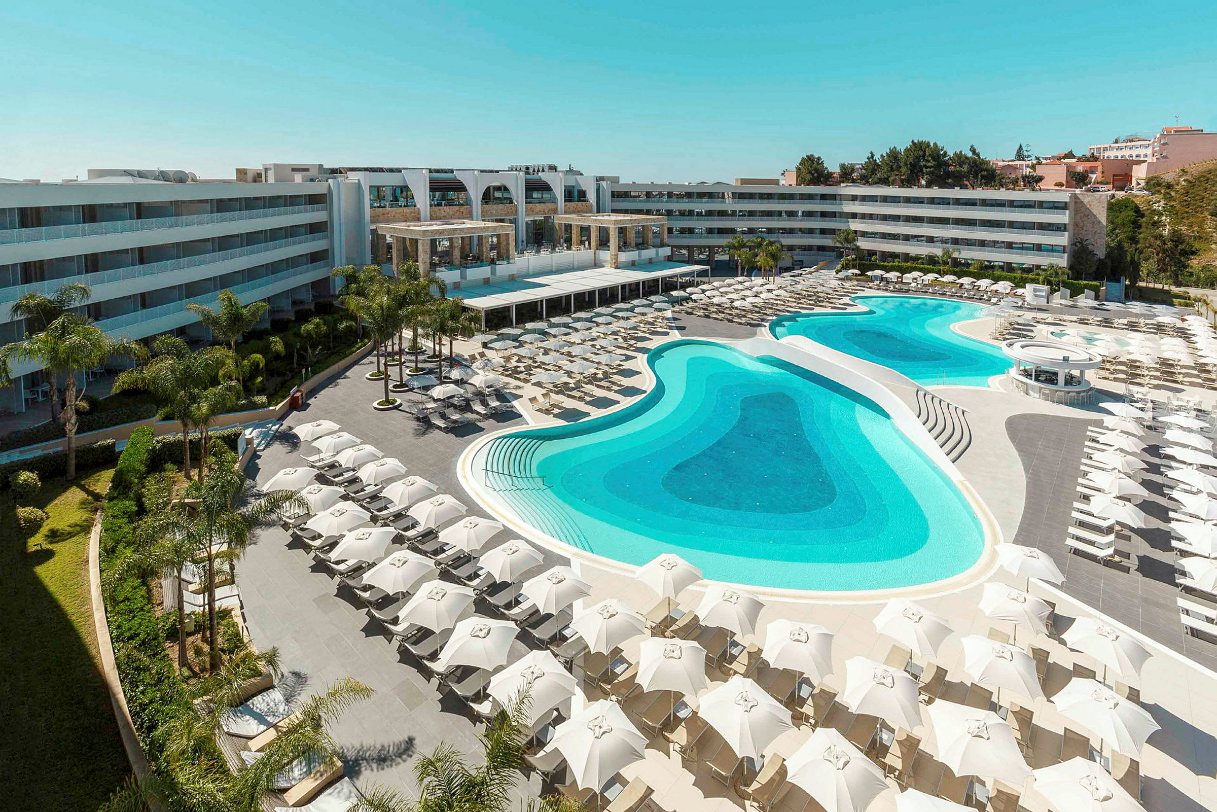 Billede af et hotelområde med stor pool og liggestole. (AI-genereret tekst)
