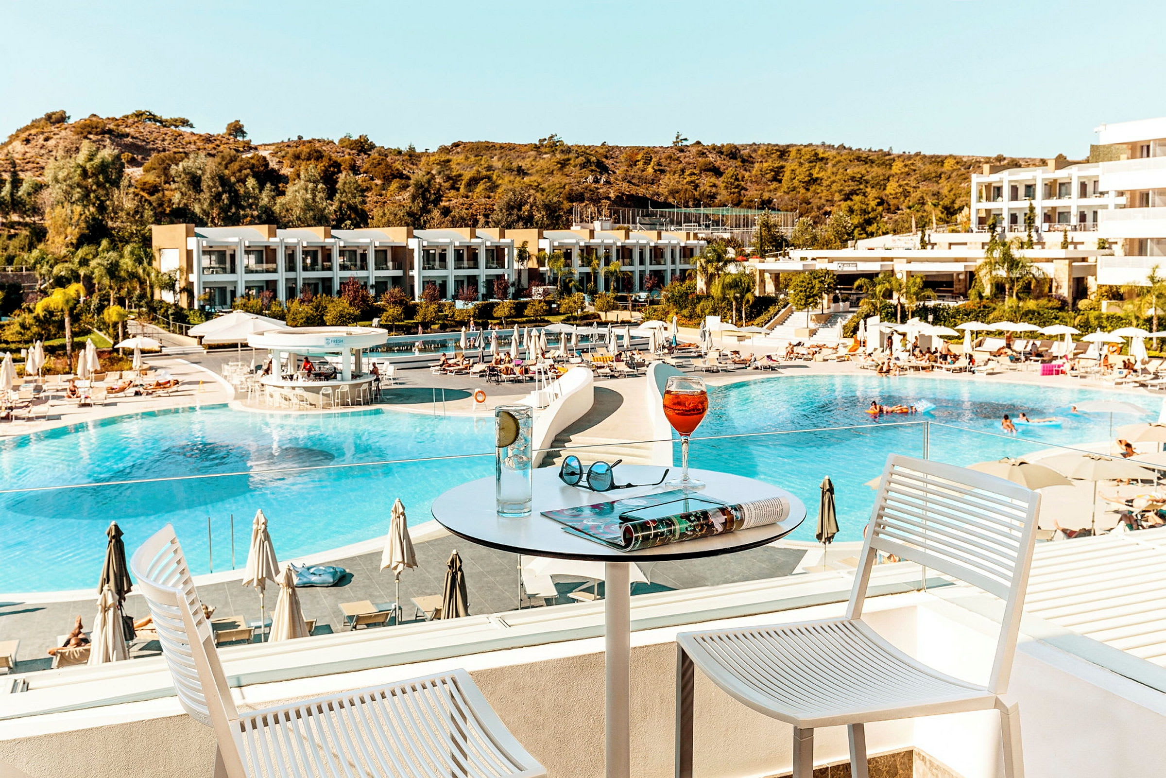 Hotellets poolområde set fra en terrasse med drikkevarer på et bord. (AI-genereret tekst)