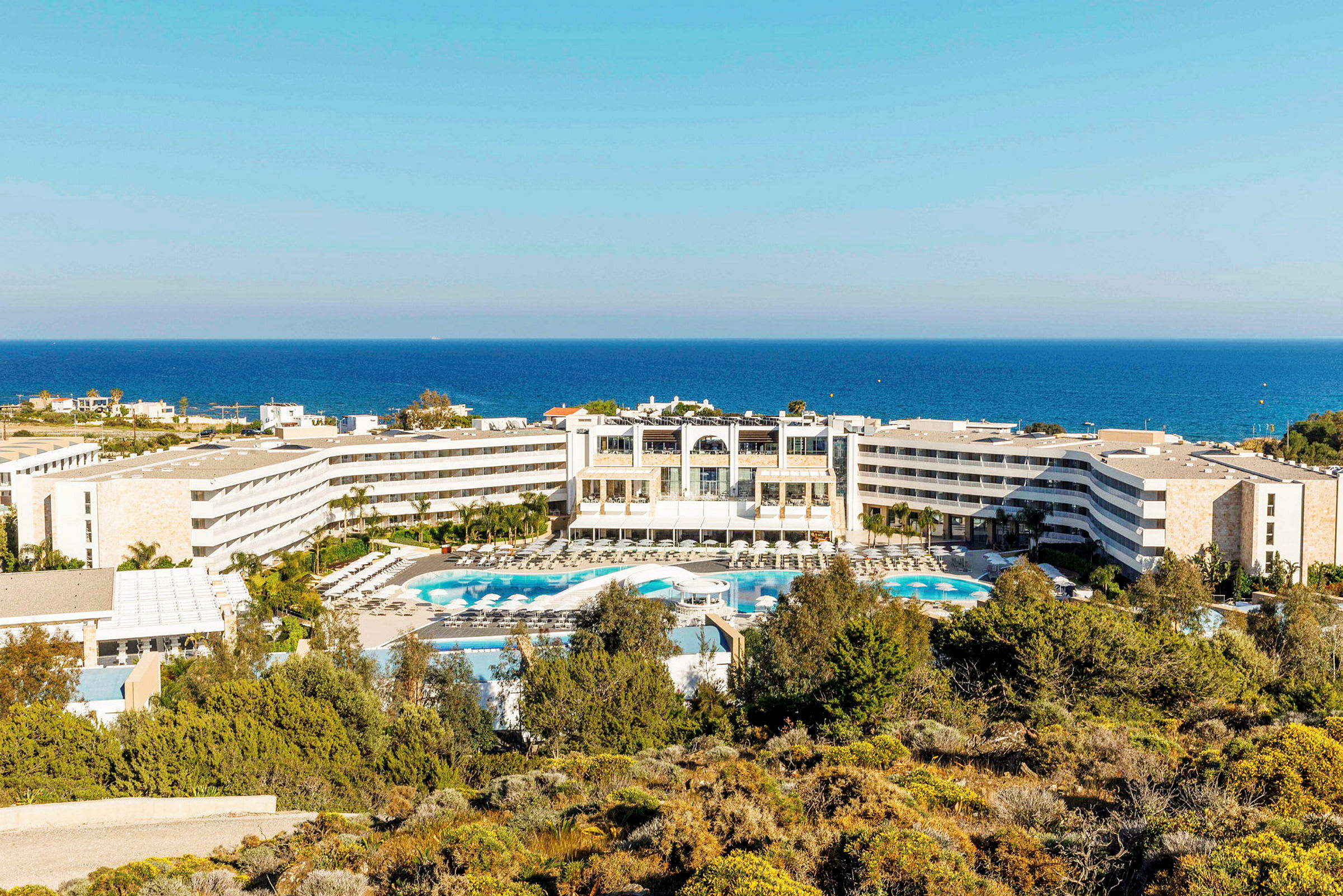 Udsigt over hotel med poolområde og havet i baggrunden. (AI-genereret tekst)