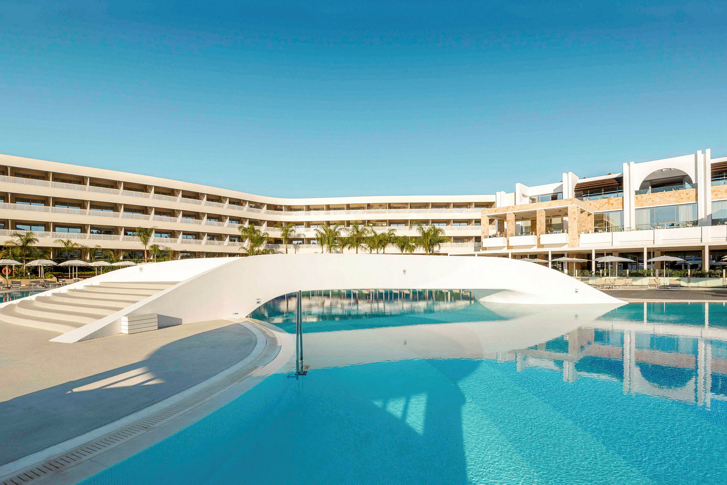 Et moderne hotel med en stor pool og en hvid bro over vandet. (AI-genereret tekst)