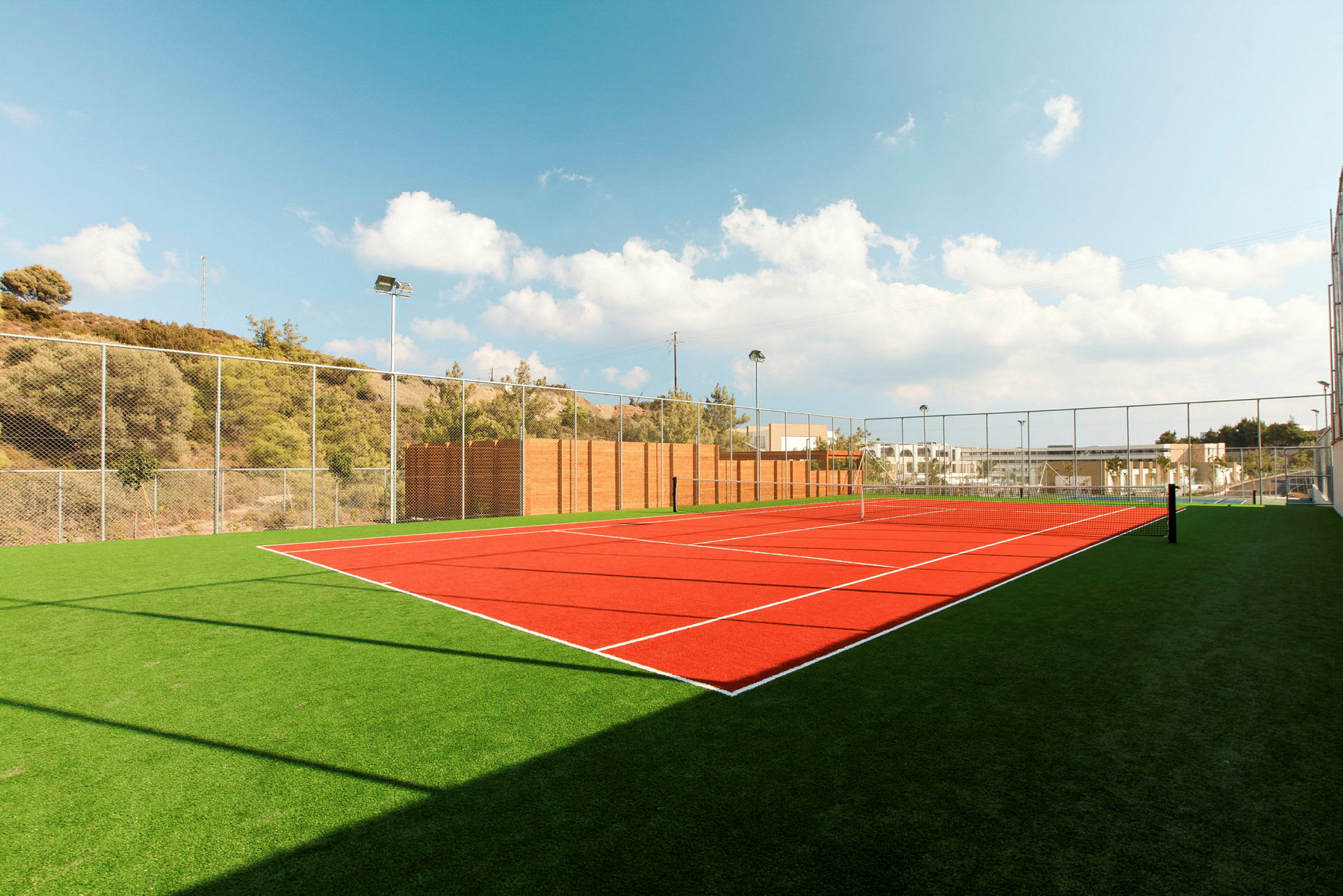 Billede af en udendørs tennisbane med kunstgræs og net under en klar blå himmel. (AI-genereret tekst)
