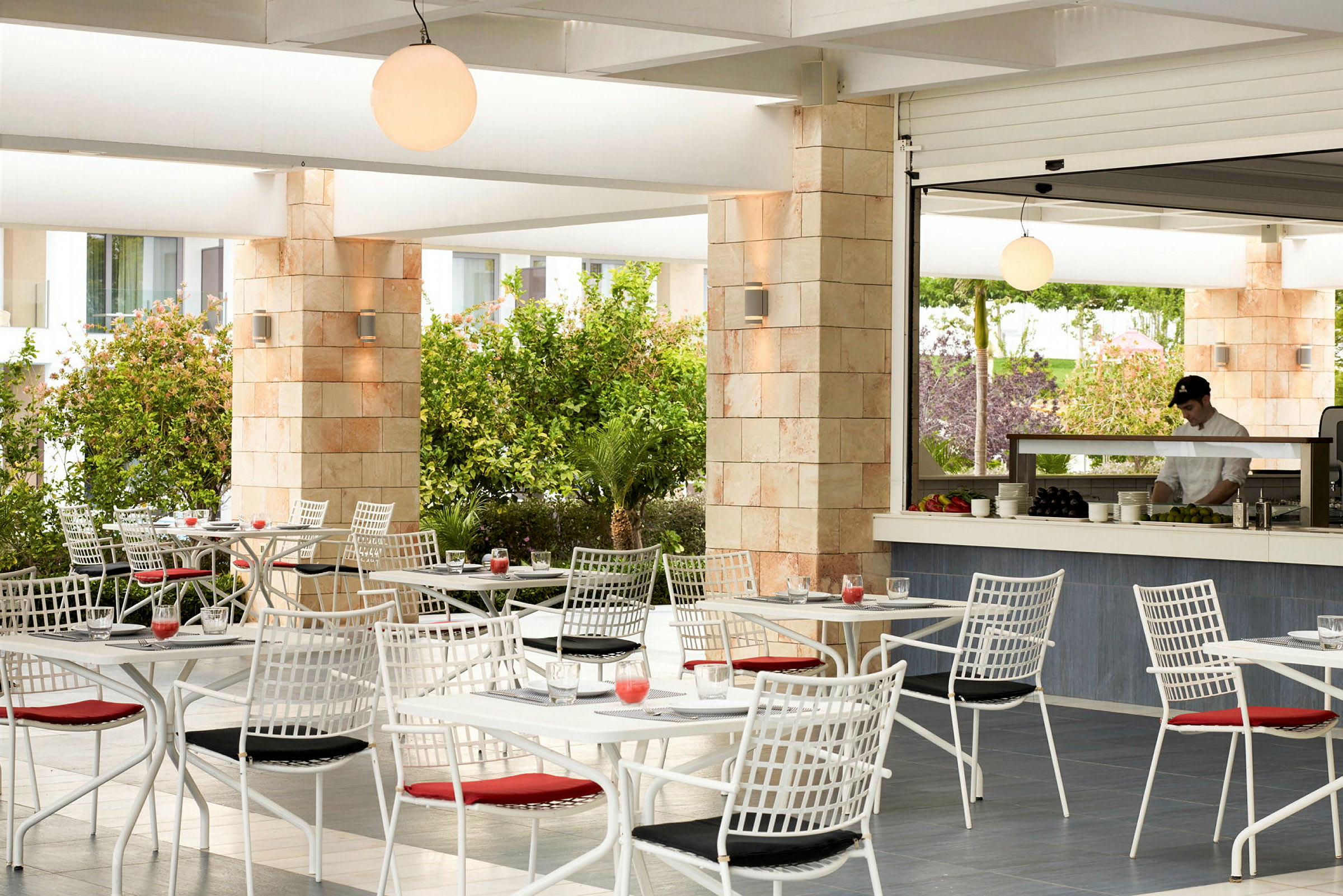 Udendørs restaurant med hvide borde og stole, omgivet af grønne planter. (AI-genereret tekst)