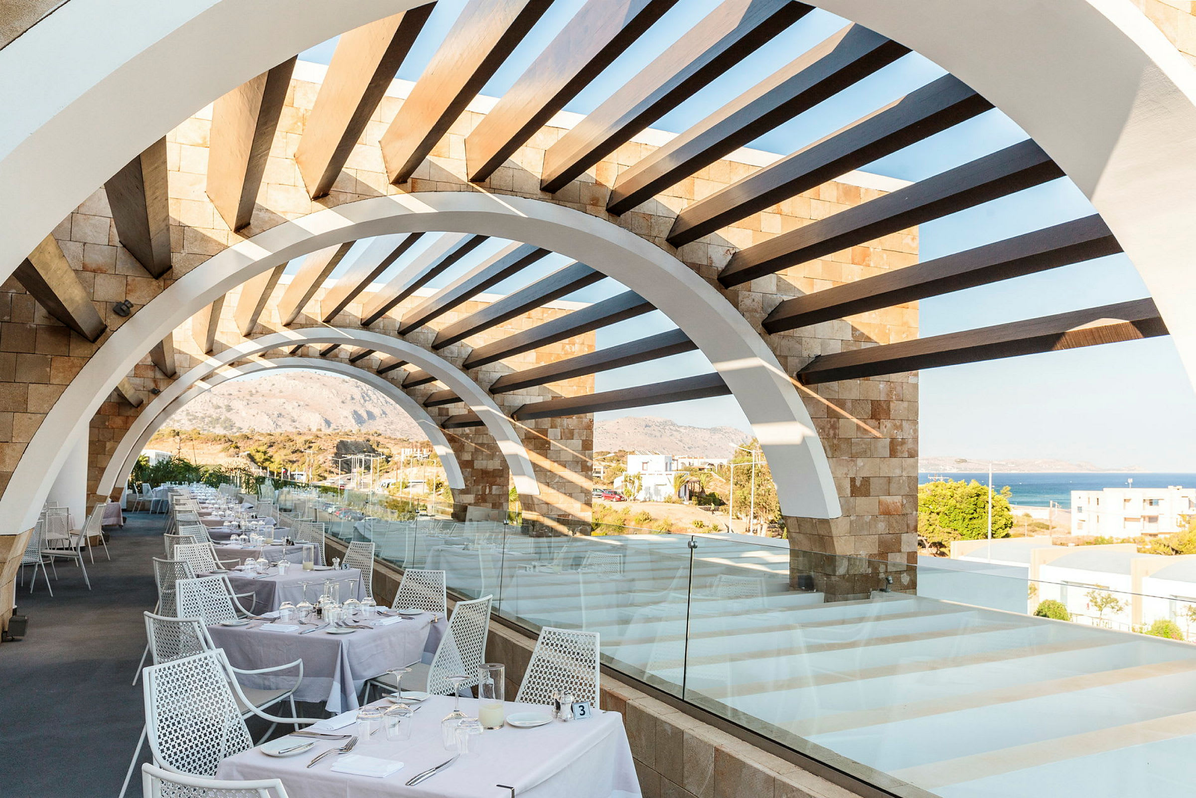 Restaurantterrasse med buet pergola og havudsigt. (AI-genereret tekst)