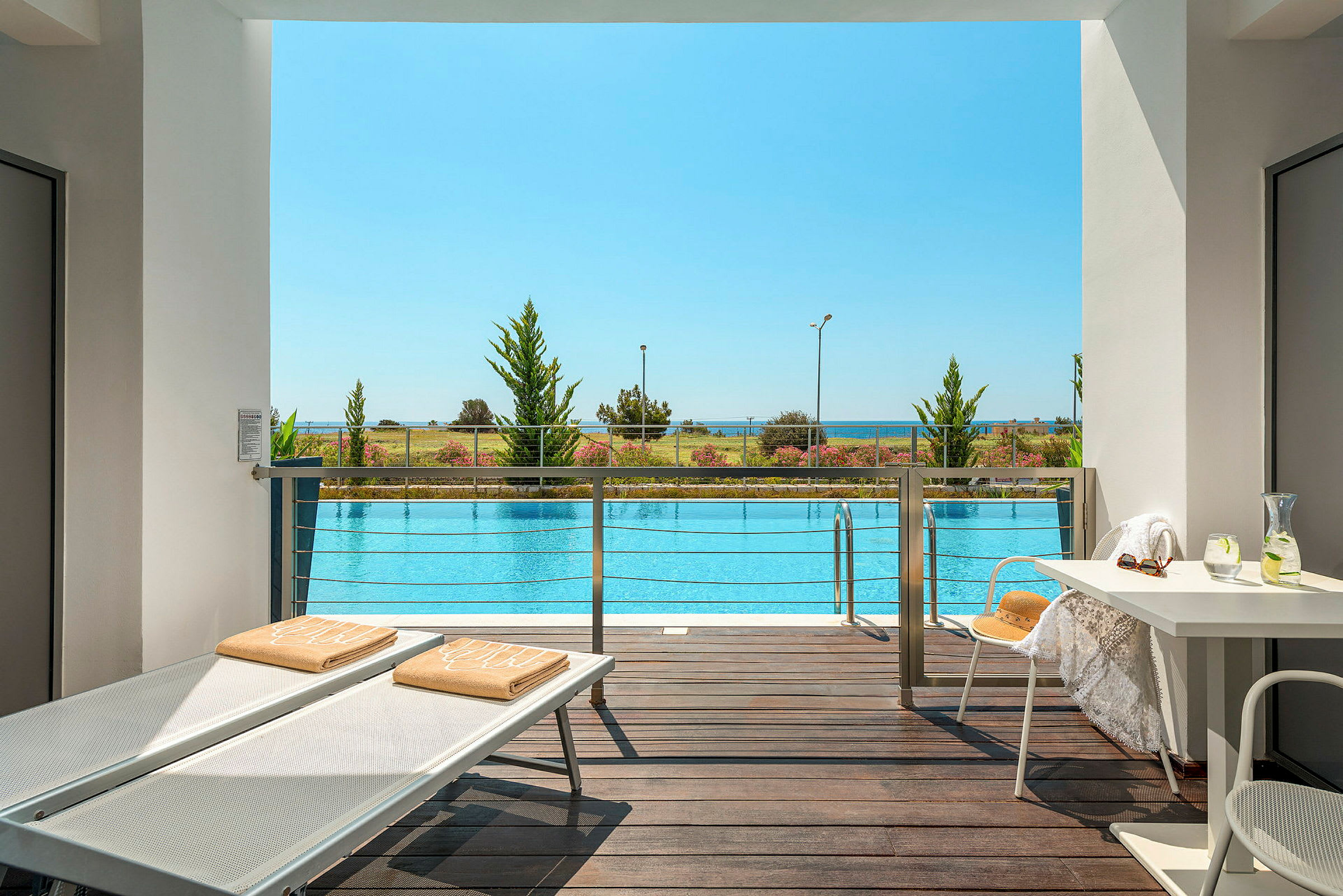 Udsigt fra terrasse over en pool med strand og hav i baggrunden. (AI-genereret tekst)