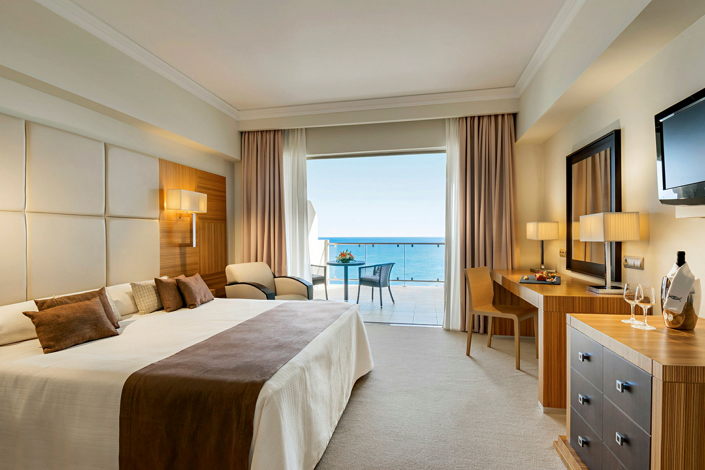 Hotelværelse med stor dobbeltseng og udsigt til havet fra balkonen. (AI-genereret tekst)