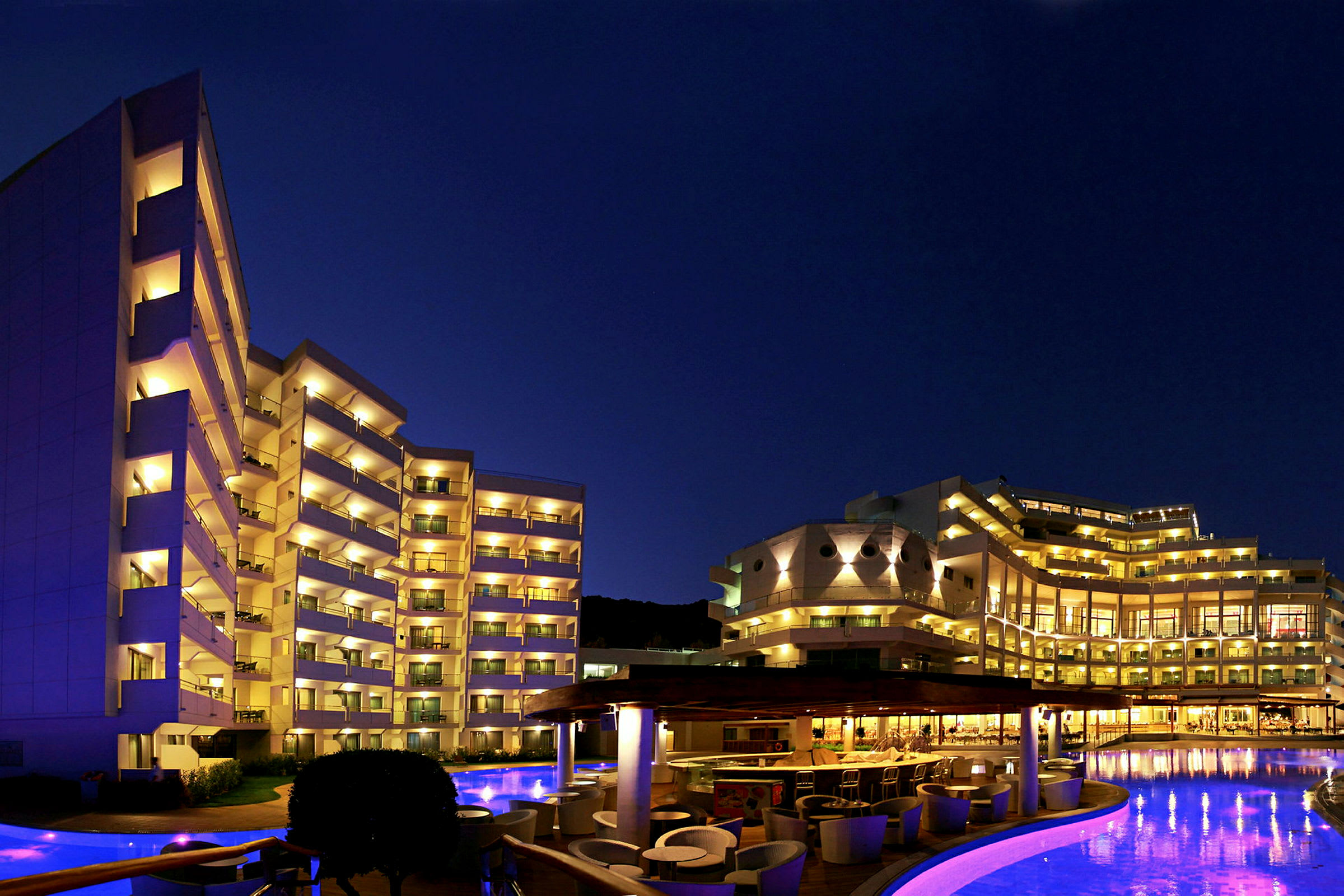 Hotel ved natbelysning med pool og udendørs område. (AI-genereret tekst)