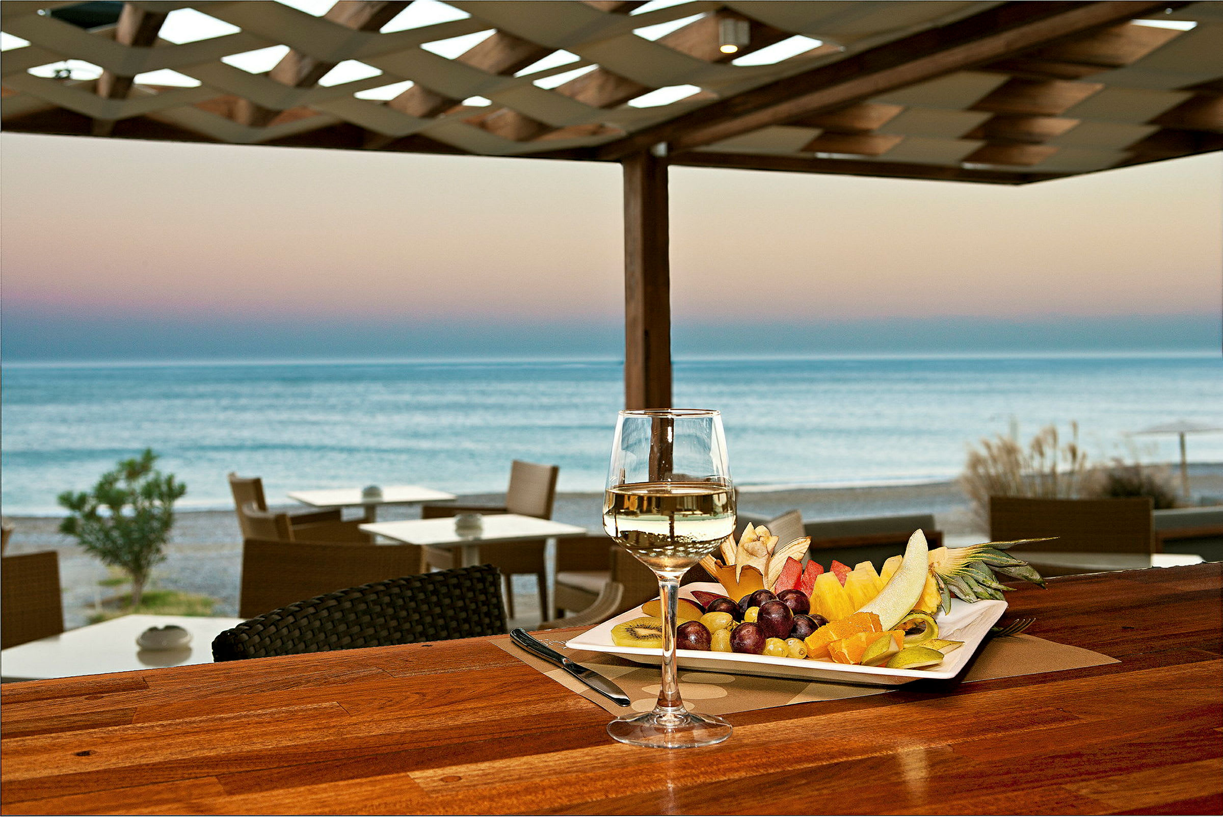 En tallerken med frisk frugt og et glas hvidvin står på et bord med udsigt over havet. (AI-genereret tekst)