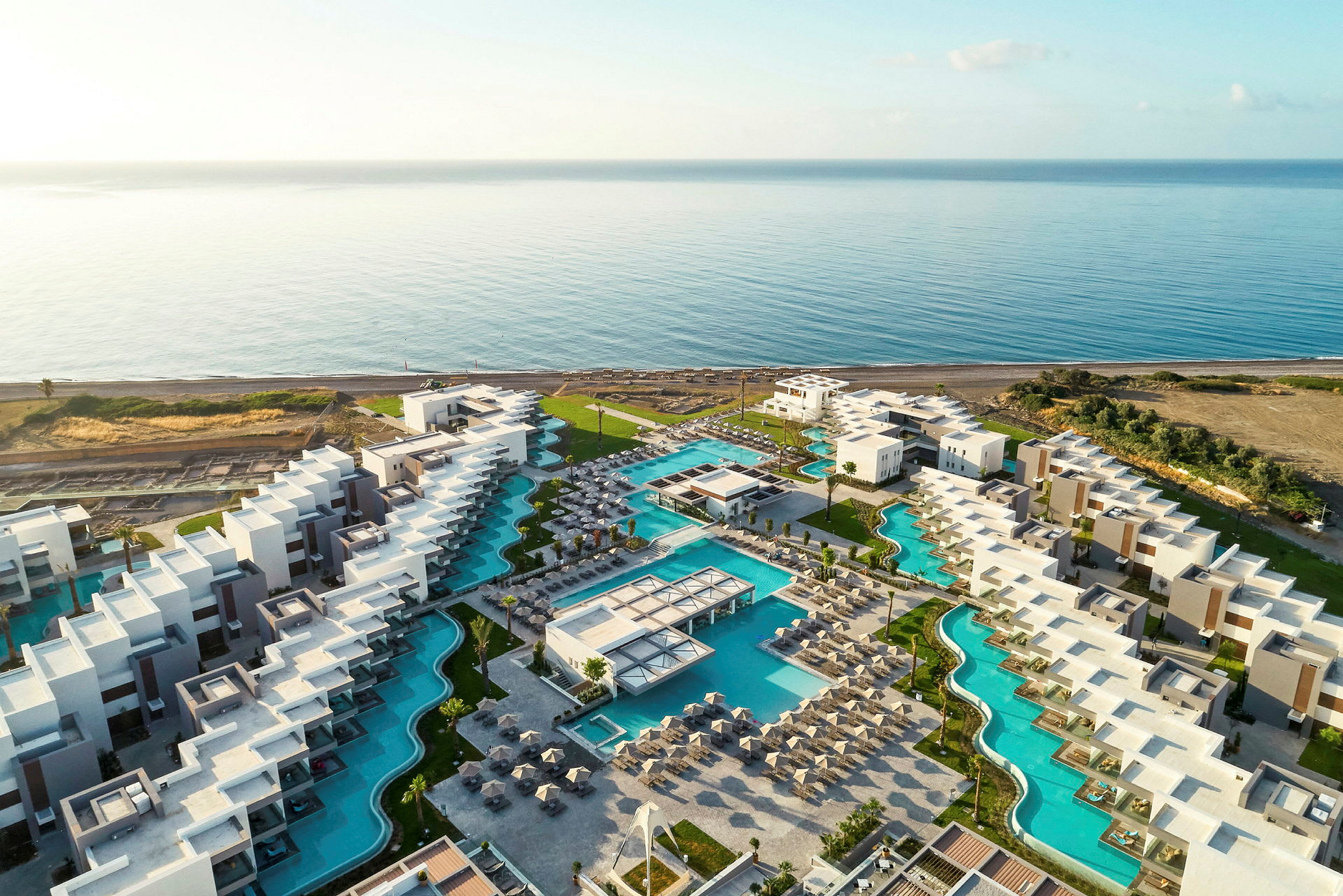 Luftfoto af en hotelresort med swimmingpools nær havet. (AI-genereret tekst)
