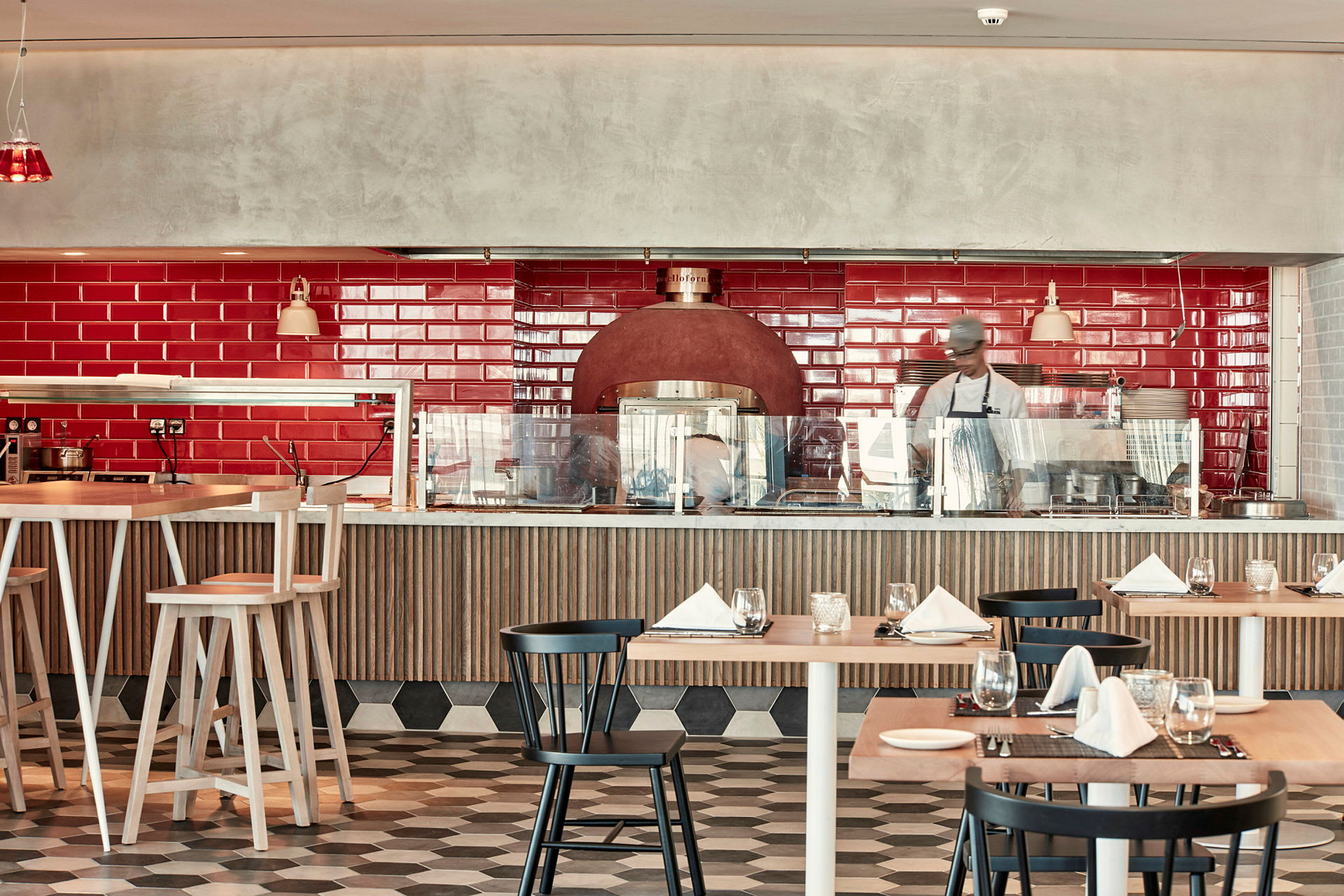 En restaurantinteriør med rød flisebelagt væg, spiseborde og stole samt en brændeovn. (AI-genereret tekst)