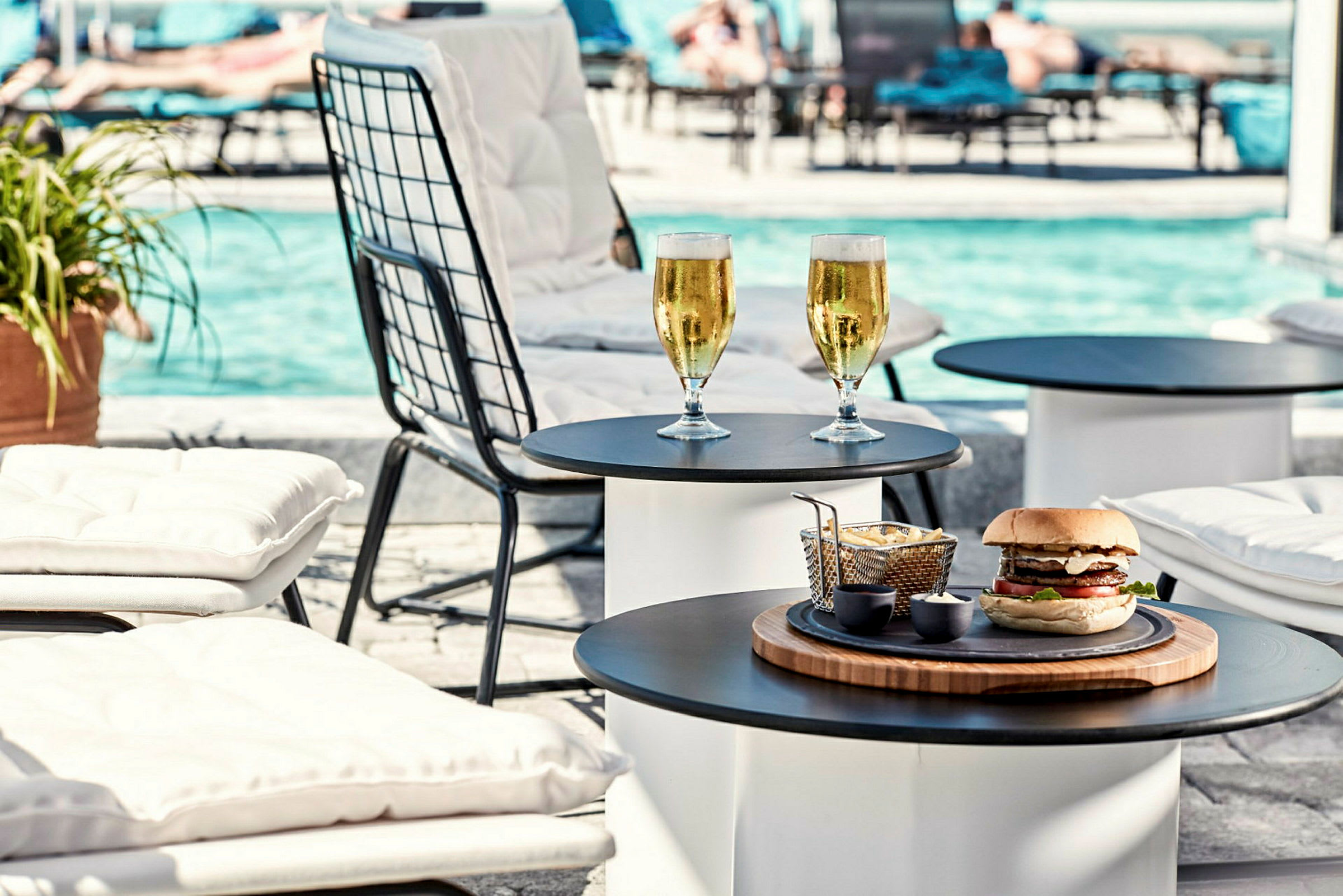 Liggestole ved en pool med drikkevarer og burger på et bord. (AI-genereret tekst)