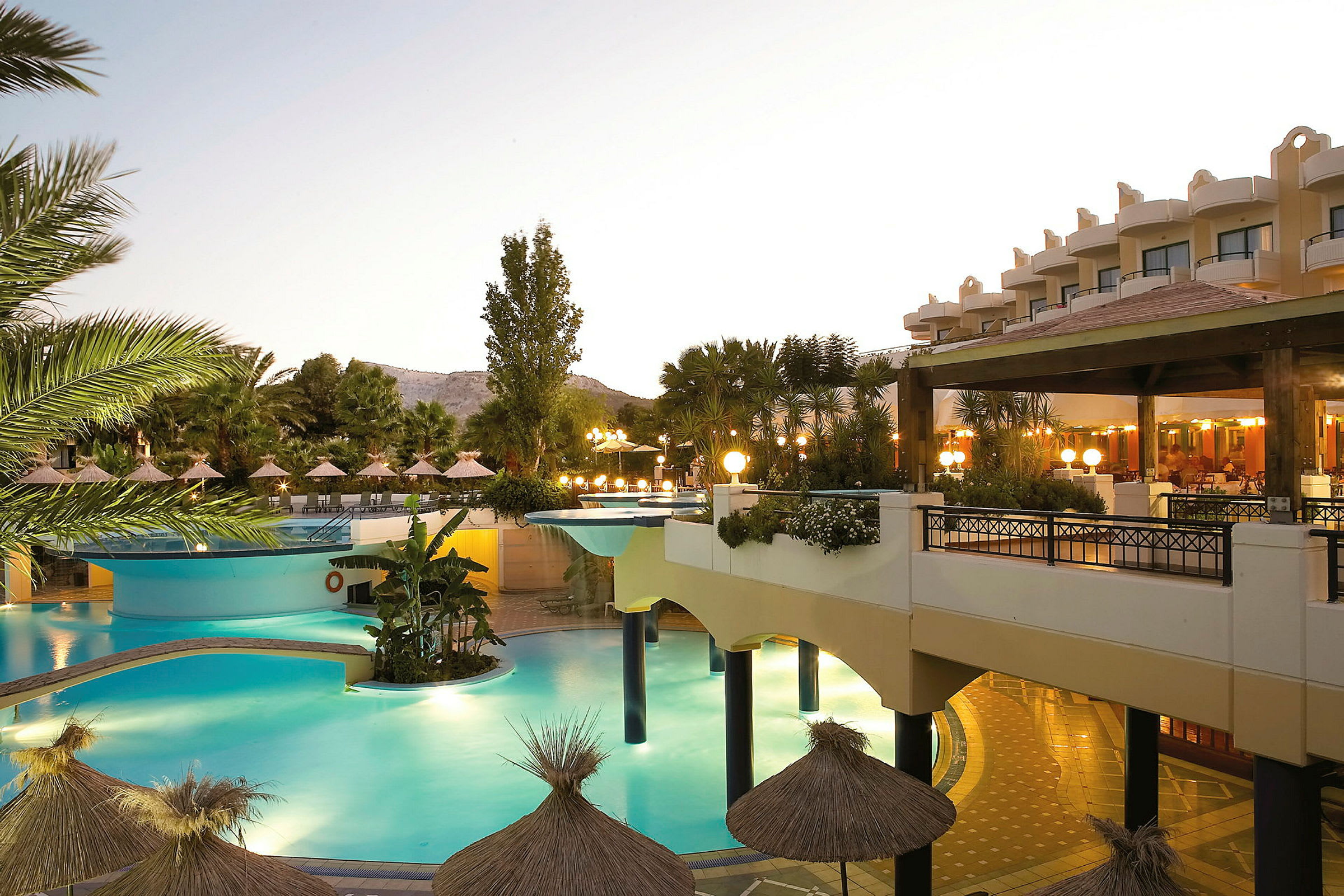En udendørs pool ved en resort, omgivet af parasoller og grøn beplantning. (AI-genereret tekst)