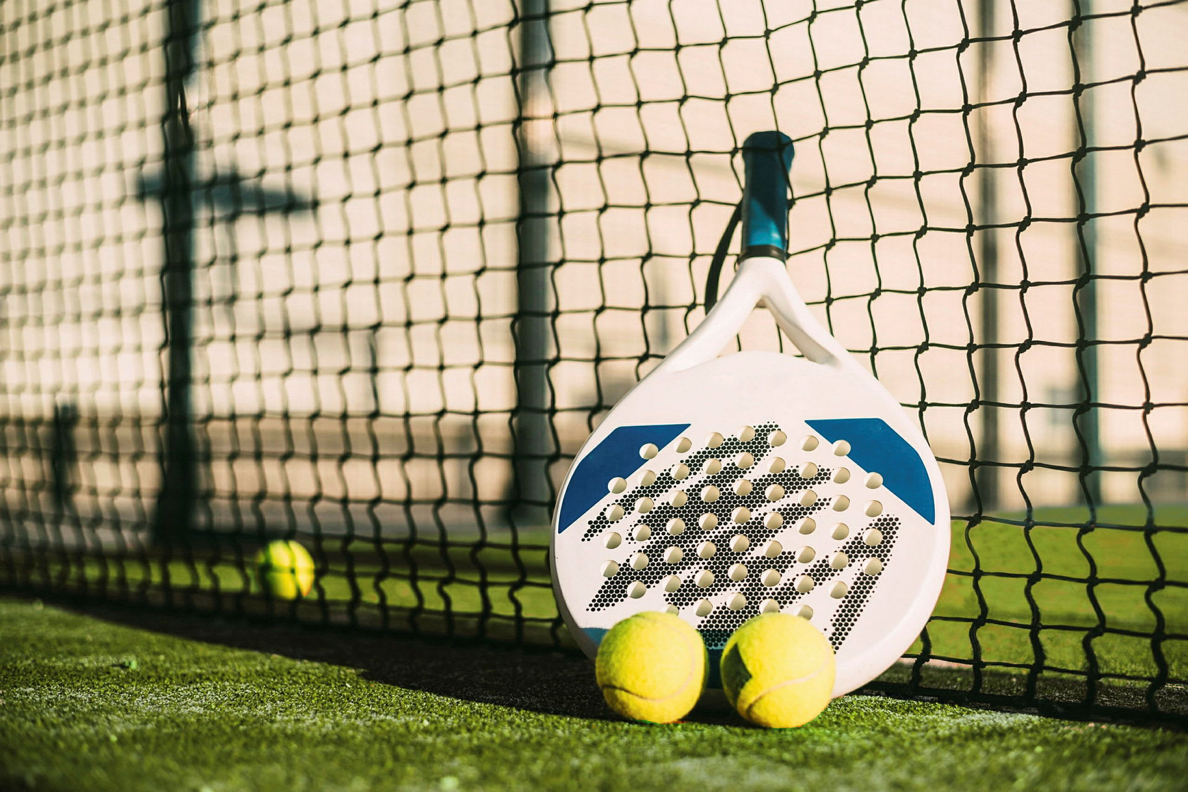 En padelbat og to bolde ved nettet på en padelbane. (AI-genereret tekst)
