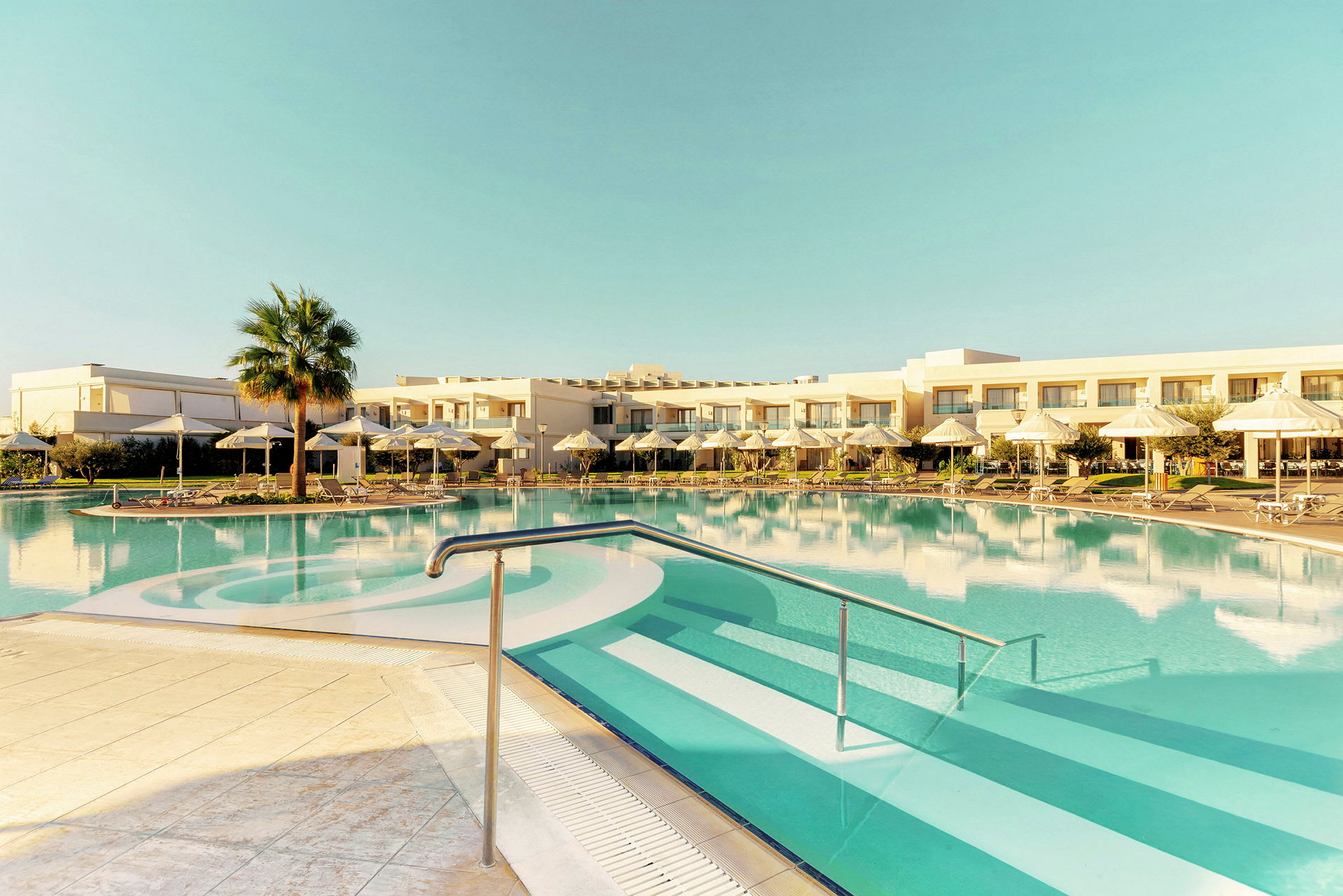 Udendørs pool med parasoller og liggestole, hotelbygning i baggrunden. (AI-genereret tekst)
