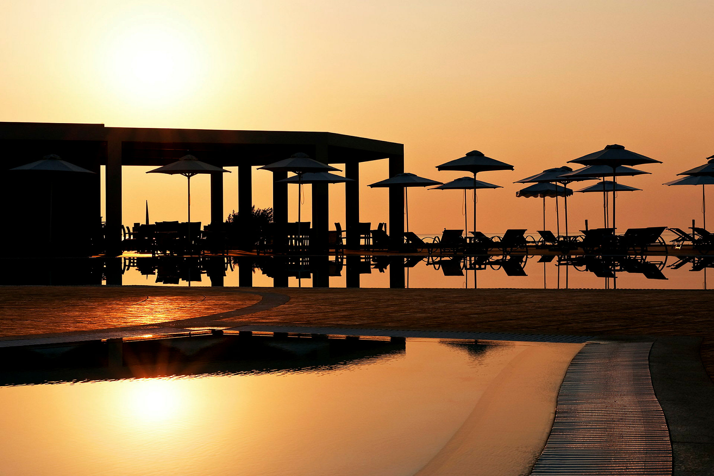 Solnedgang ved en pool med liggestole og parasoller. (AI-genereret tekst)