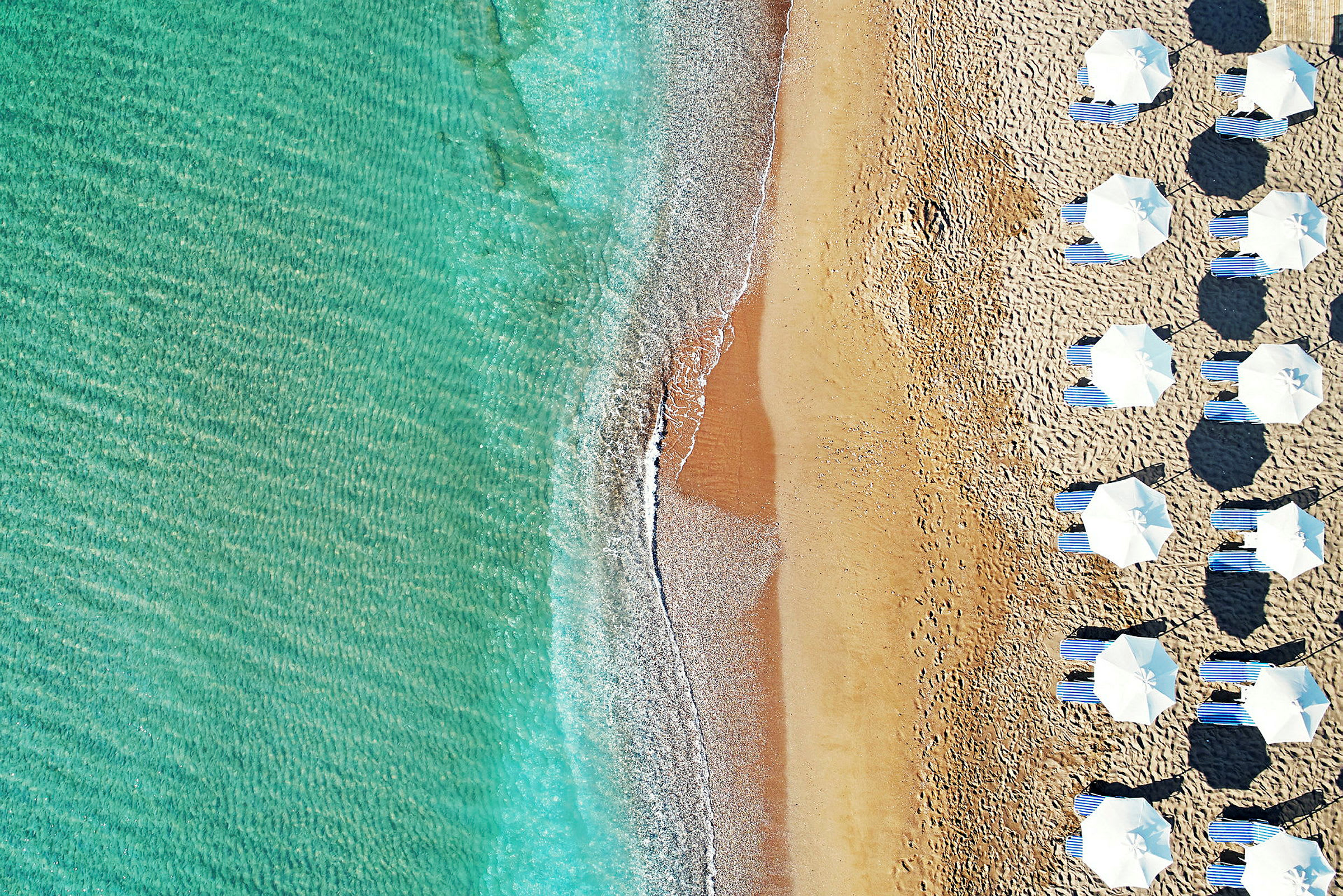 Luftfoto af en strand med parasoller og solsenge ved klart vand. (AI-genereret tekst)