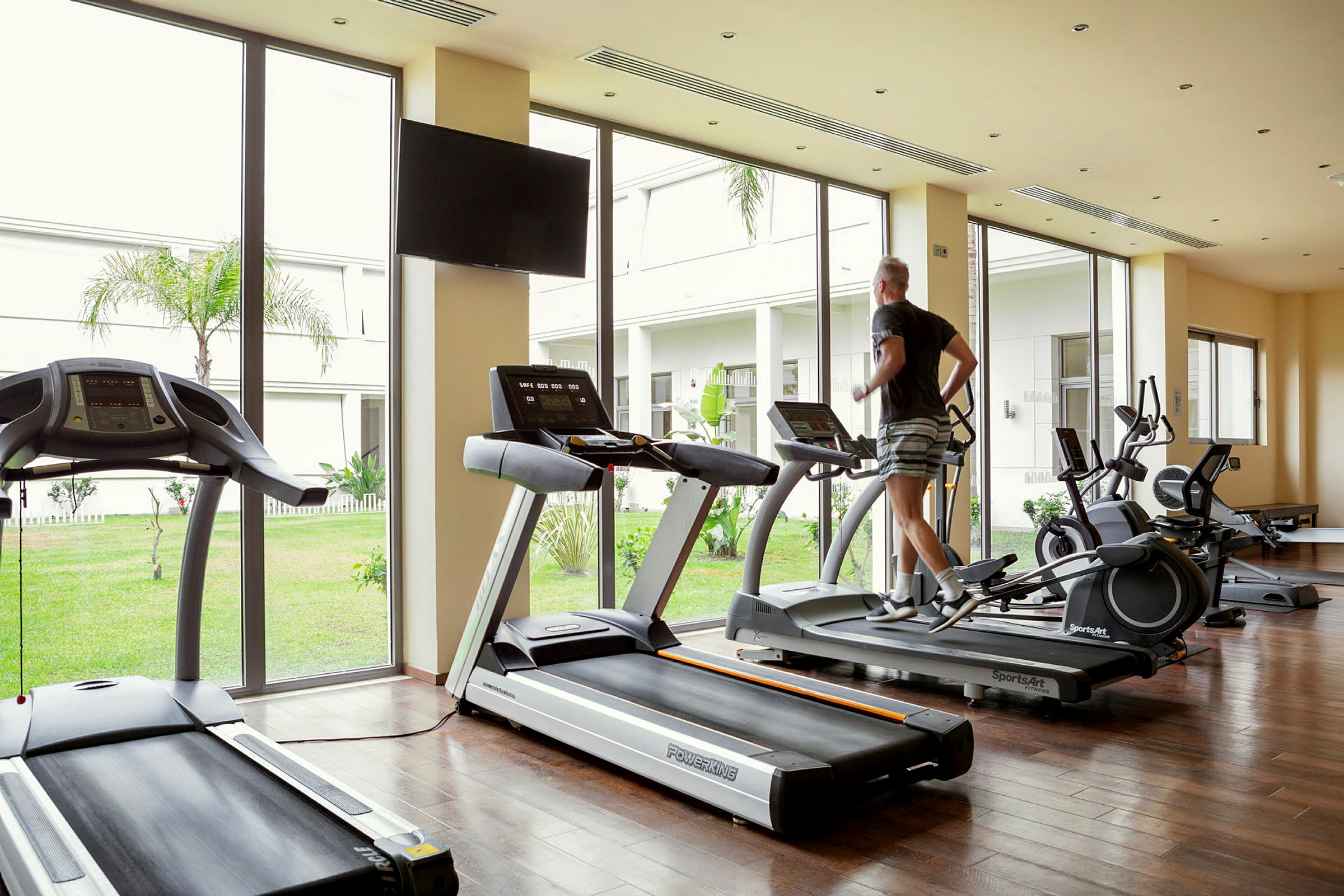 En person løber på et løbebånd i et fitnesscenter med vinduer ud til en have. (AI-genereret tekst)