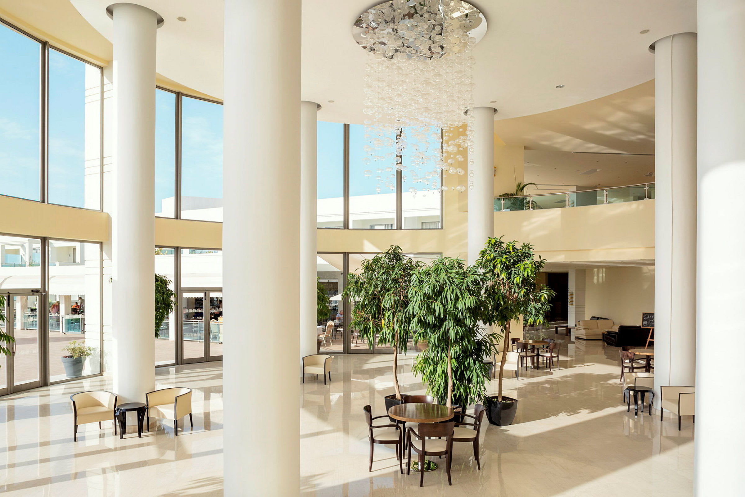 Et hotelatrium med store vinduer, stole og borde samt grønne planter. (AI-genereret tekst)