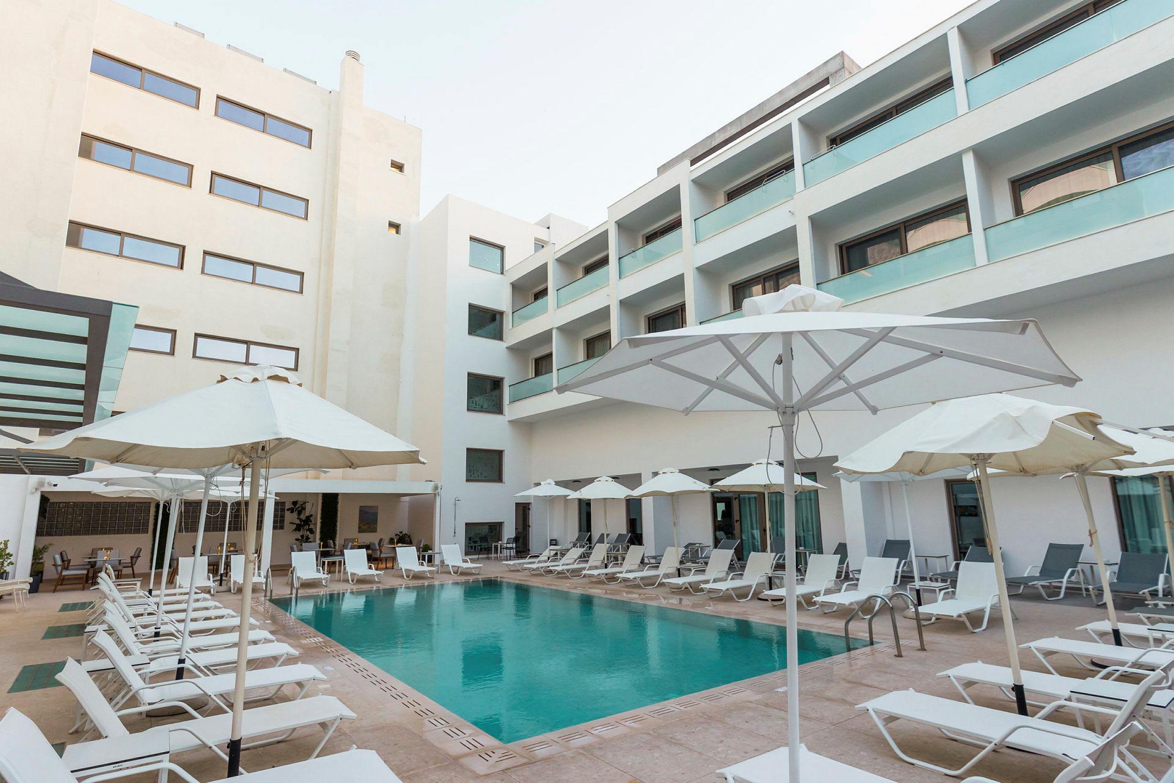 En hotelpool omgivet af liggestole og parasoller. (AI-genereret tekst)