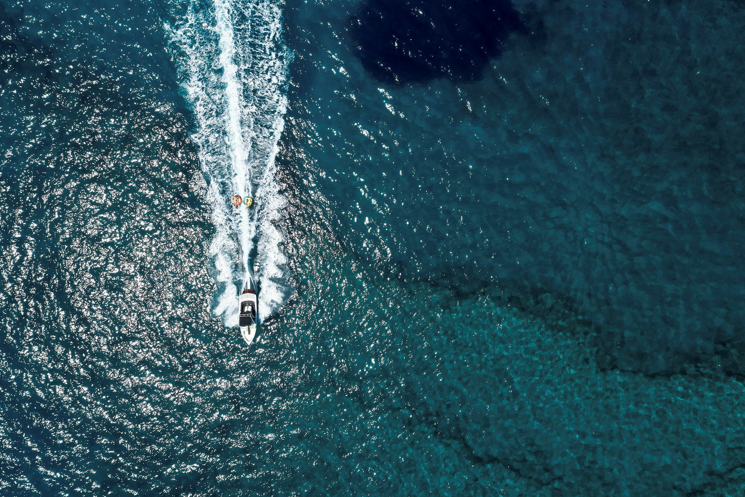 Luftbillede af en motorbåd, der trækker to oppustelige flåder på havet. (AI-genereret tekst)