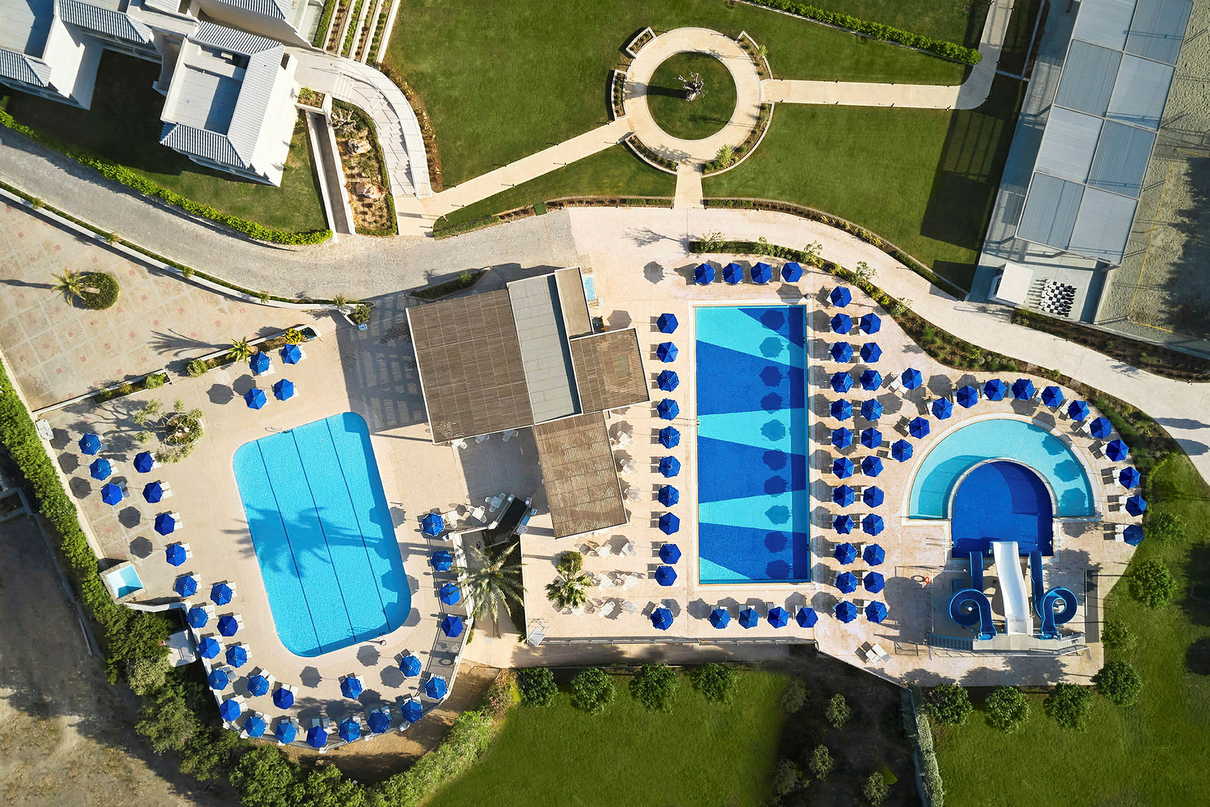 Luftfoto af et feriested med pools, liggestole og grønne områder. (AI-genereret tekst)