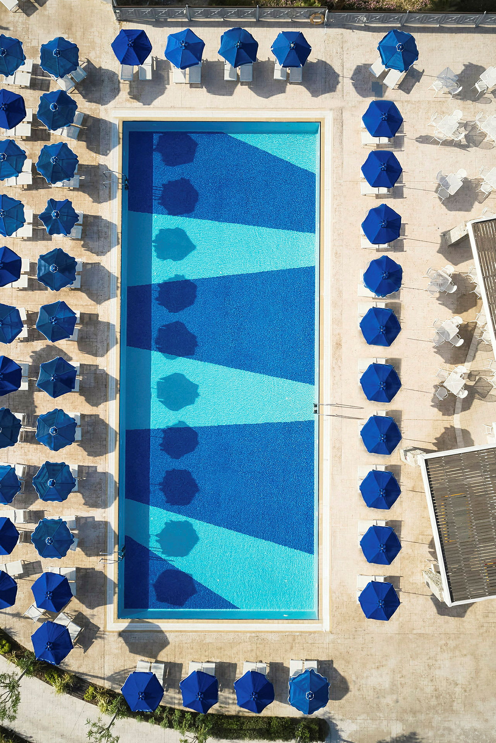 Fugleperspektiv af en swimmingpool omgivet af liggestole og parasoller. (AI-genereret tekst)