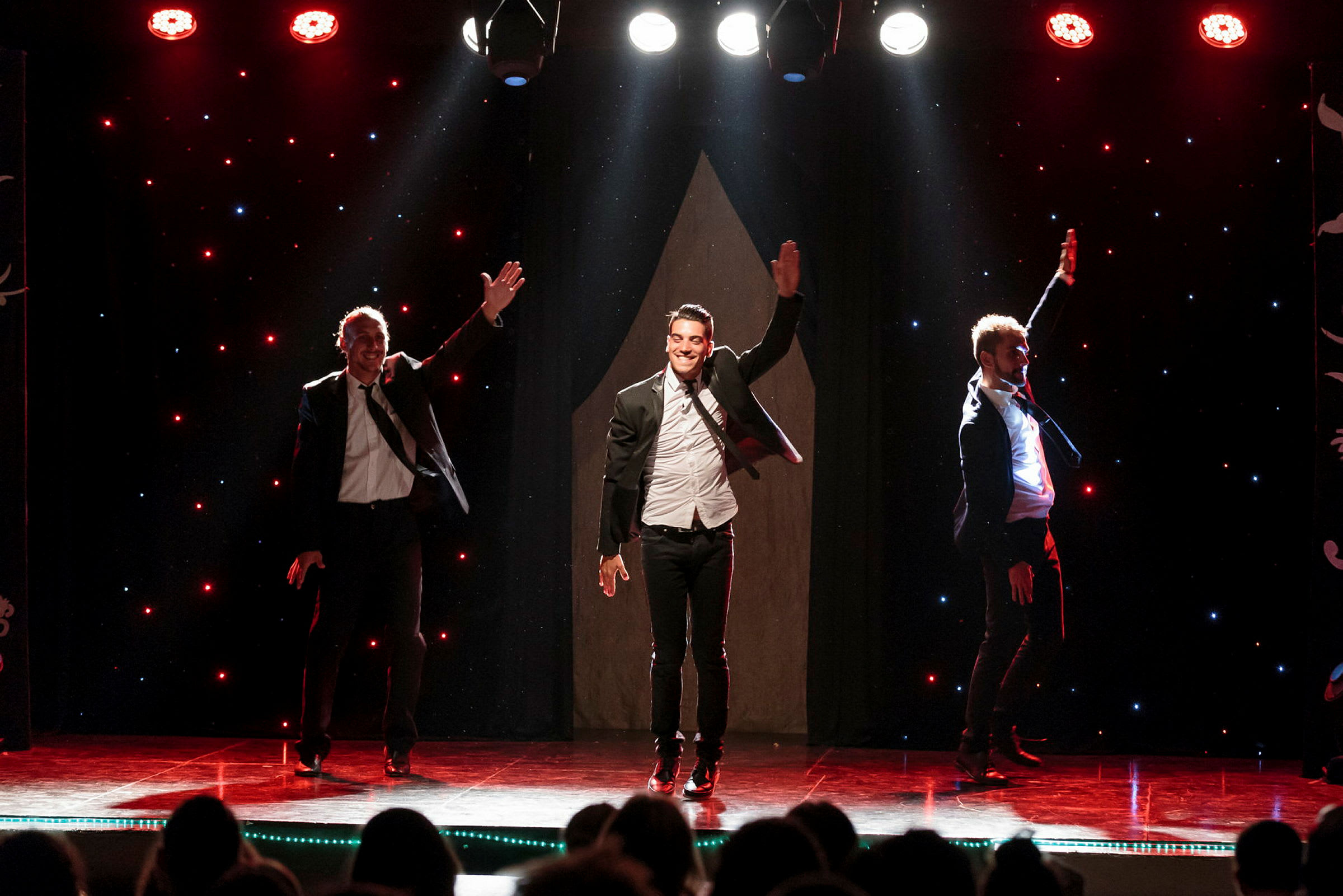 Tre personer udfører en danseforestilling på en scene med lyseffekter. (AI-genereret tekst)