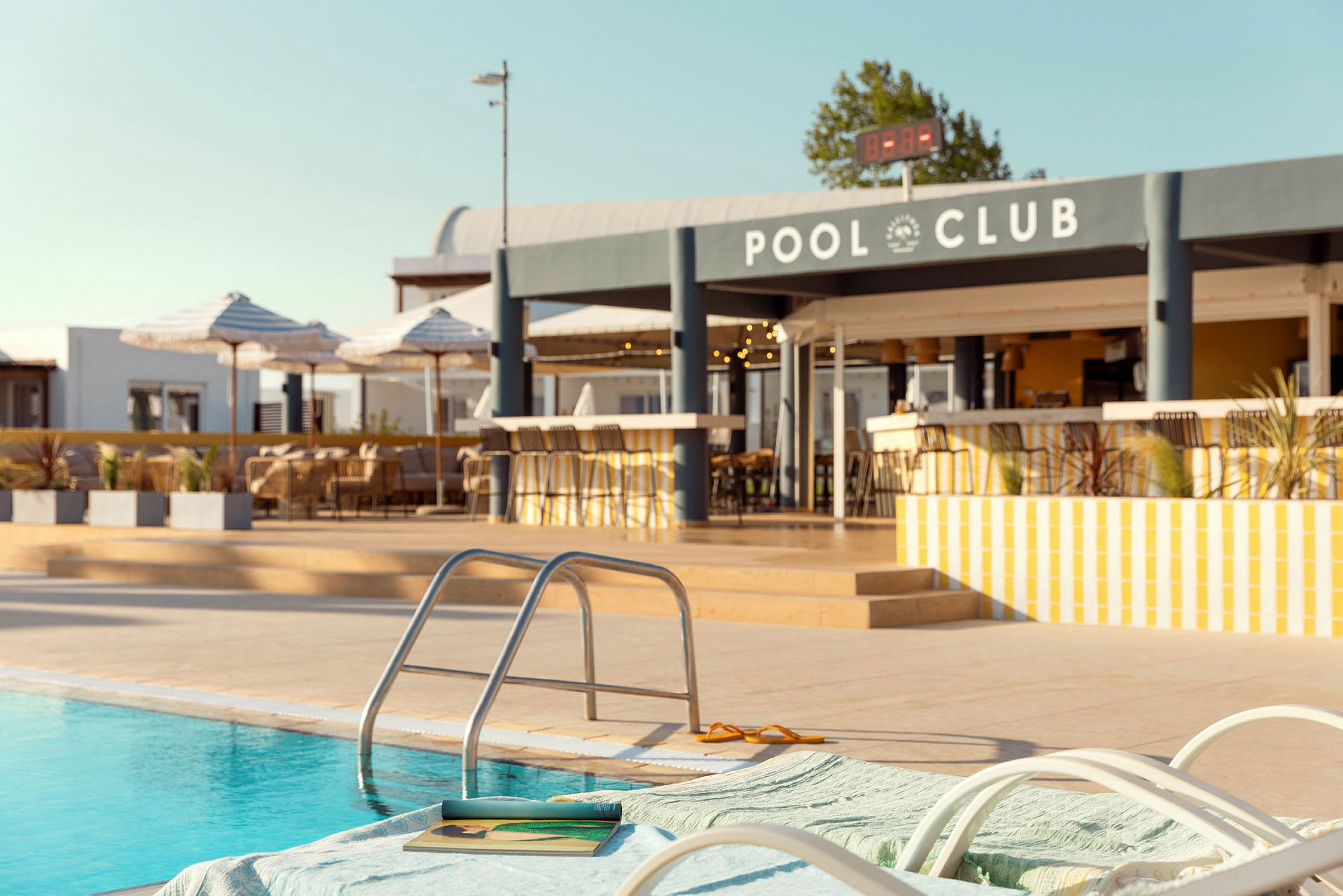 En swimmingpool med liggestole og en bar i baggrunden. (AI-genereret tekst)