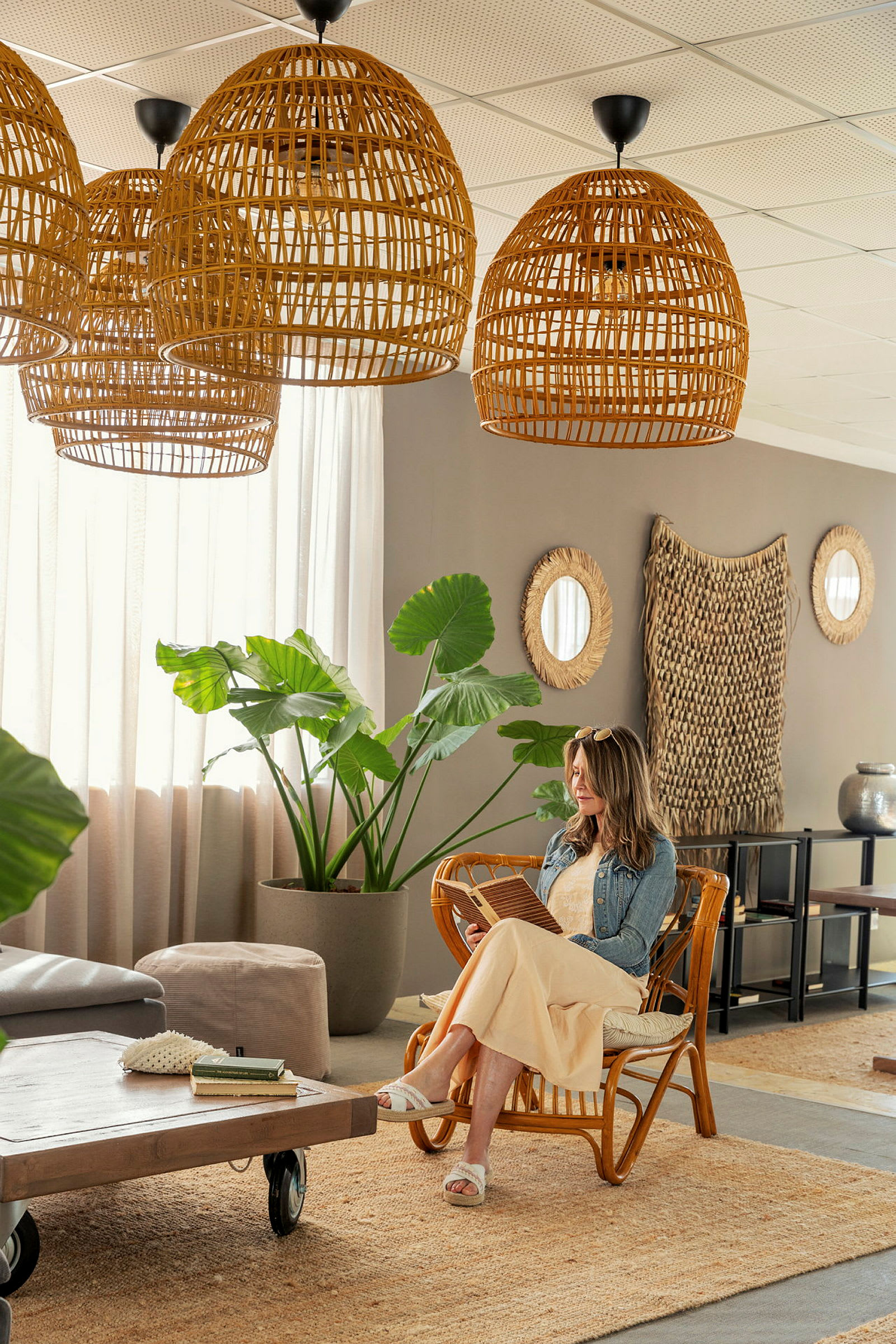 Et stilfuldt rum med møbler af rattan, store grønne planter og dekorative kurvelamper. (AI-genereret tekst)