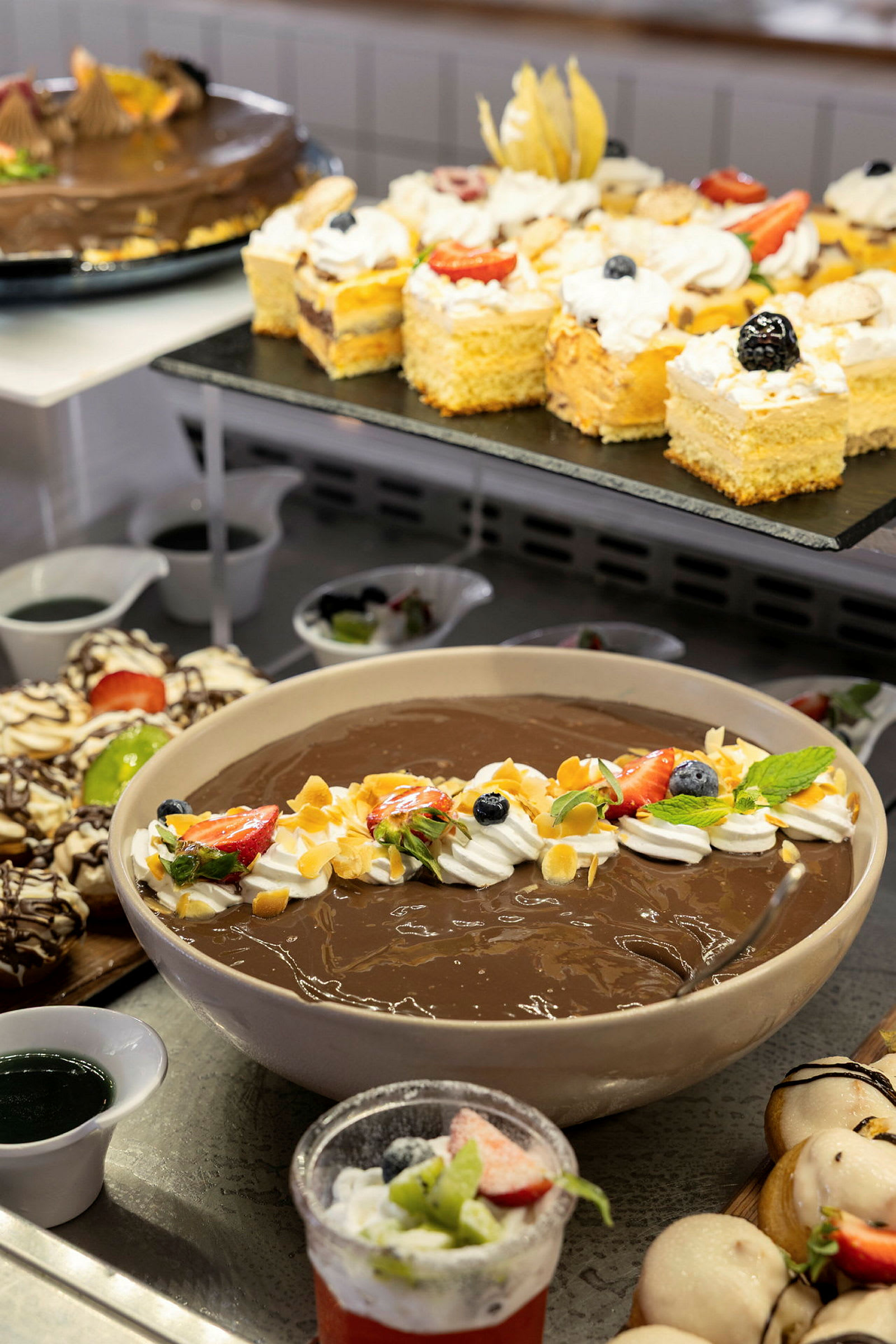 En buffet med forskellige desserter, herunder chokoladepudding pyntet med frugt og fløde. (AI-genereret tekst)