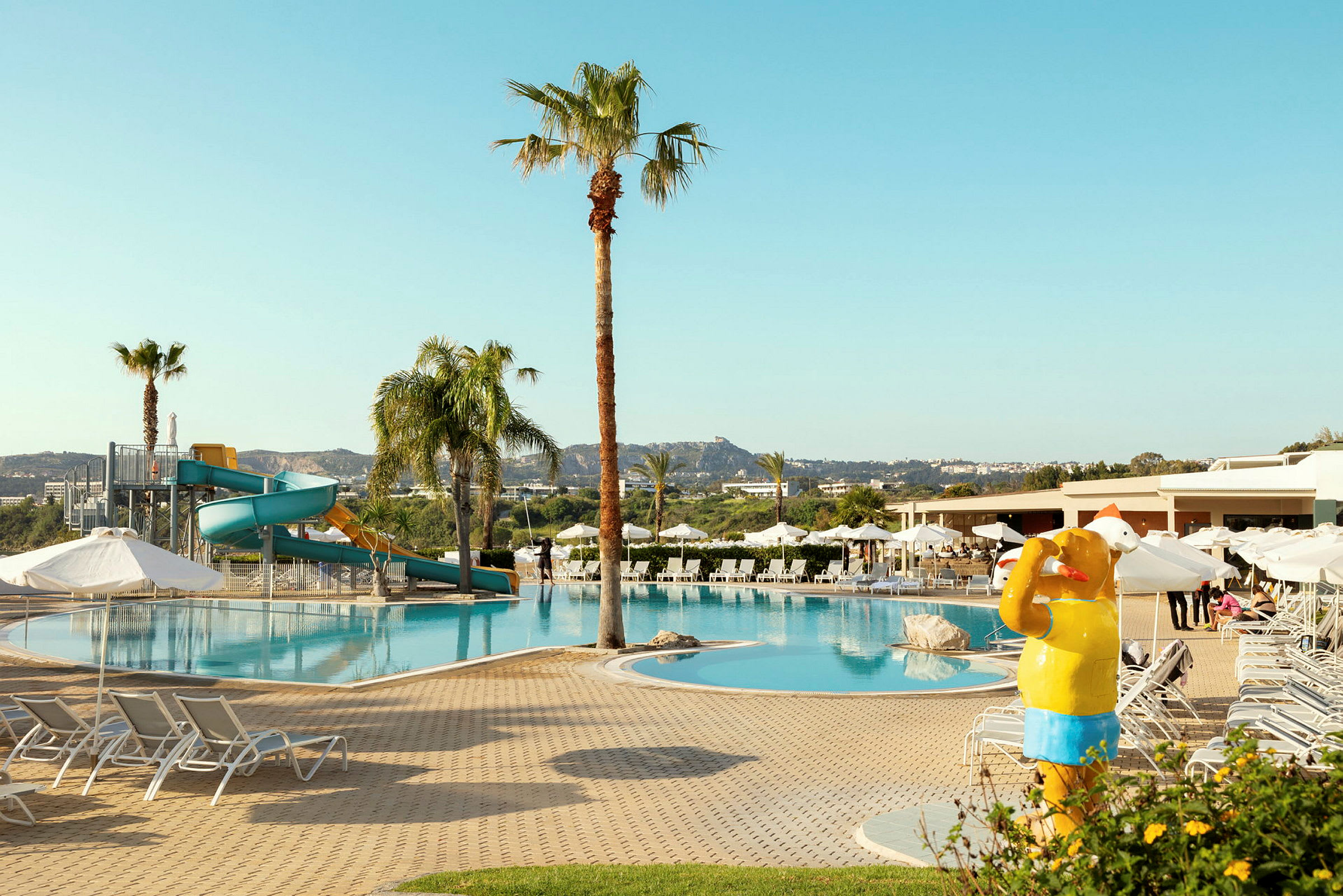 En swimmingpool med liggestole, en legeplads med vandrutsjebane og en gul skulptur, der forestiller en person der bader. (AI-genereret tekst)