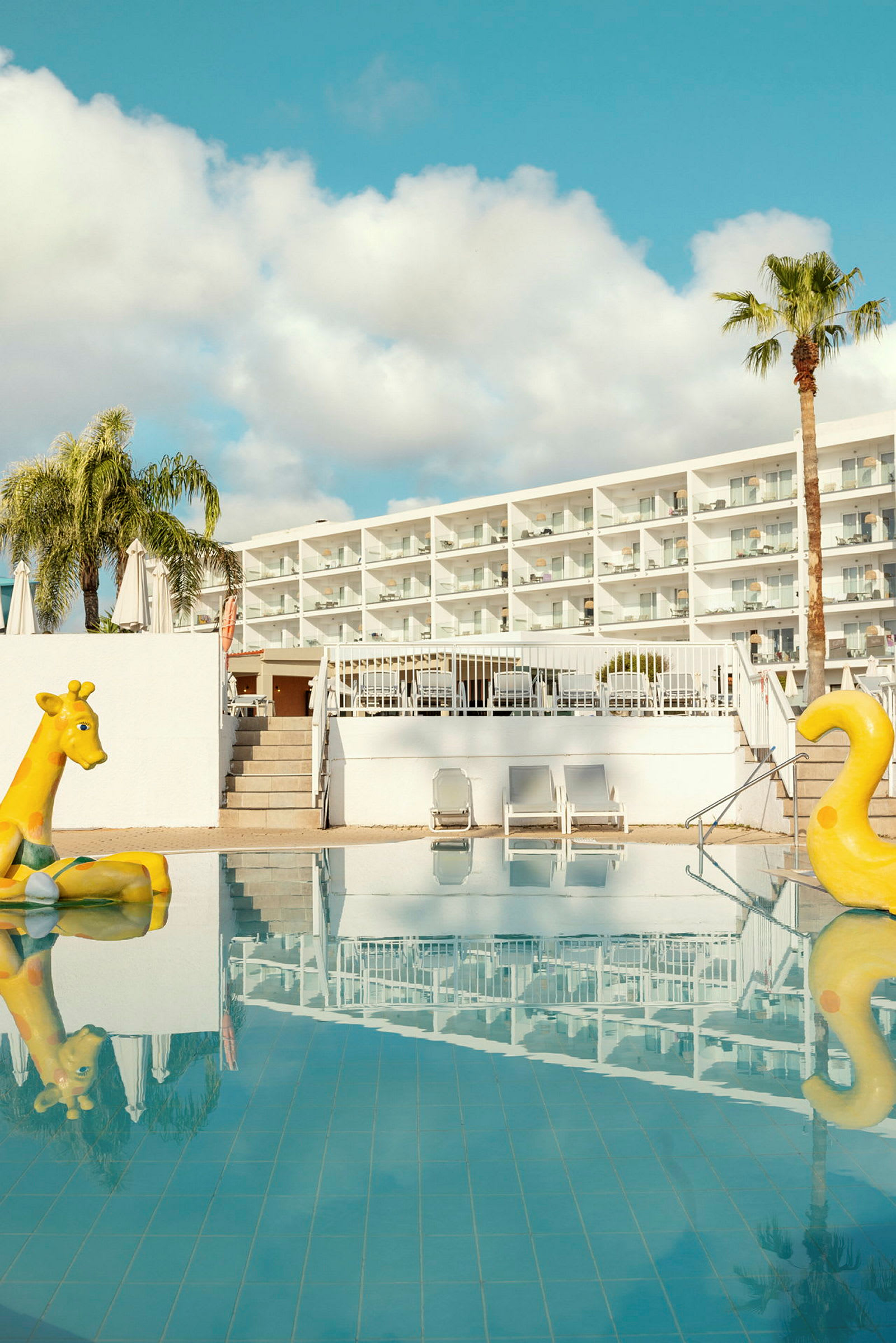 Billede af et hotel med en pool med to gule oppustelige legetøj. (AI-genereret tekst)