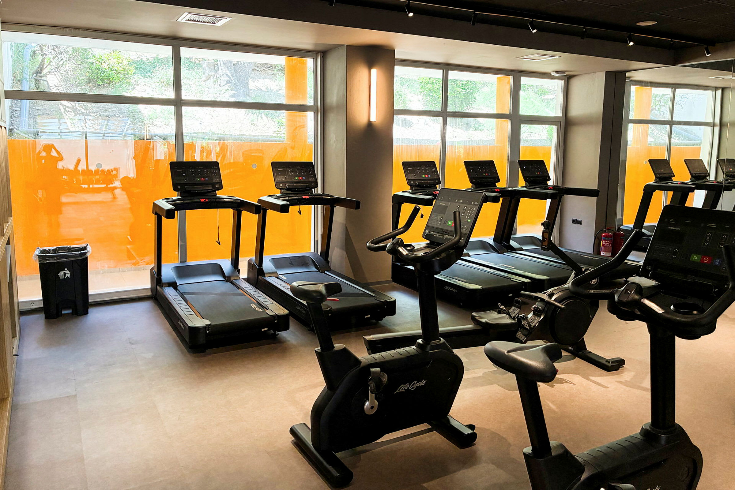 Et fitnesscenter med løbebånd og motionscykler ved store vinduer. (AI-genereret tekst)