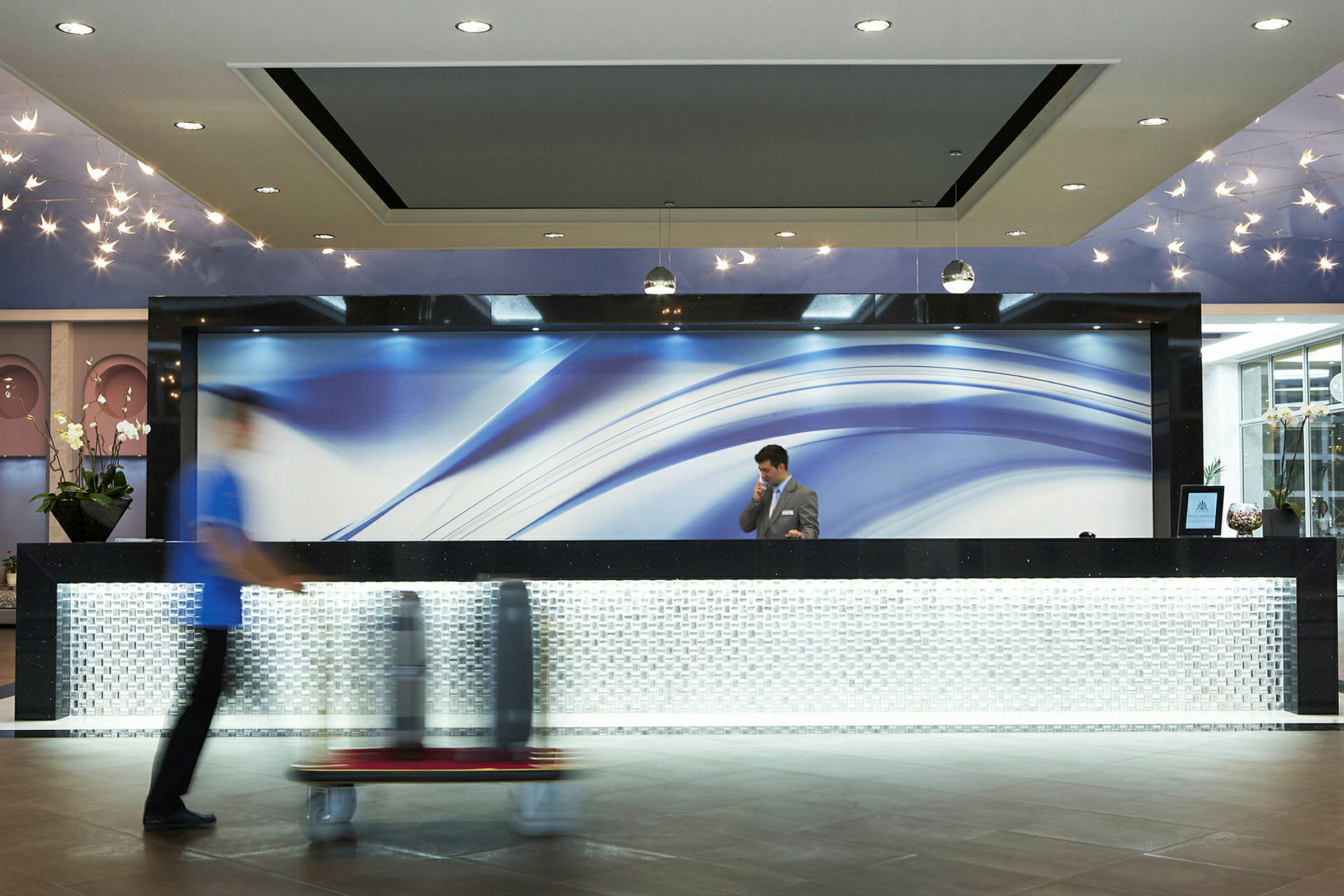 Hotellets reception med en moderne designskranke og blå baggrund på væggen. (AI-genereret tekst)