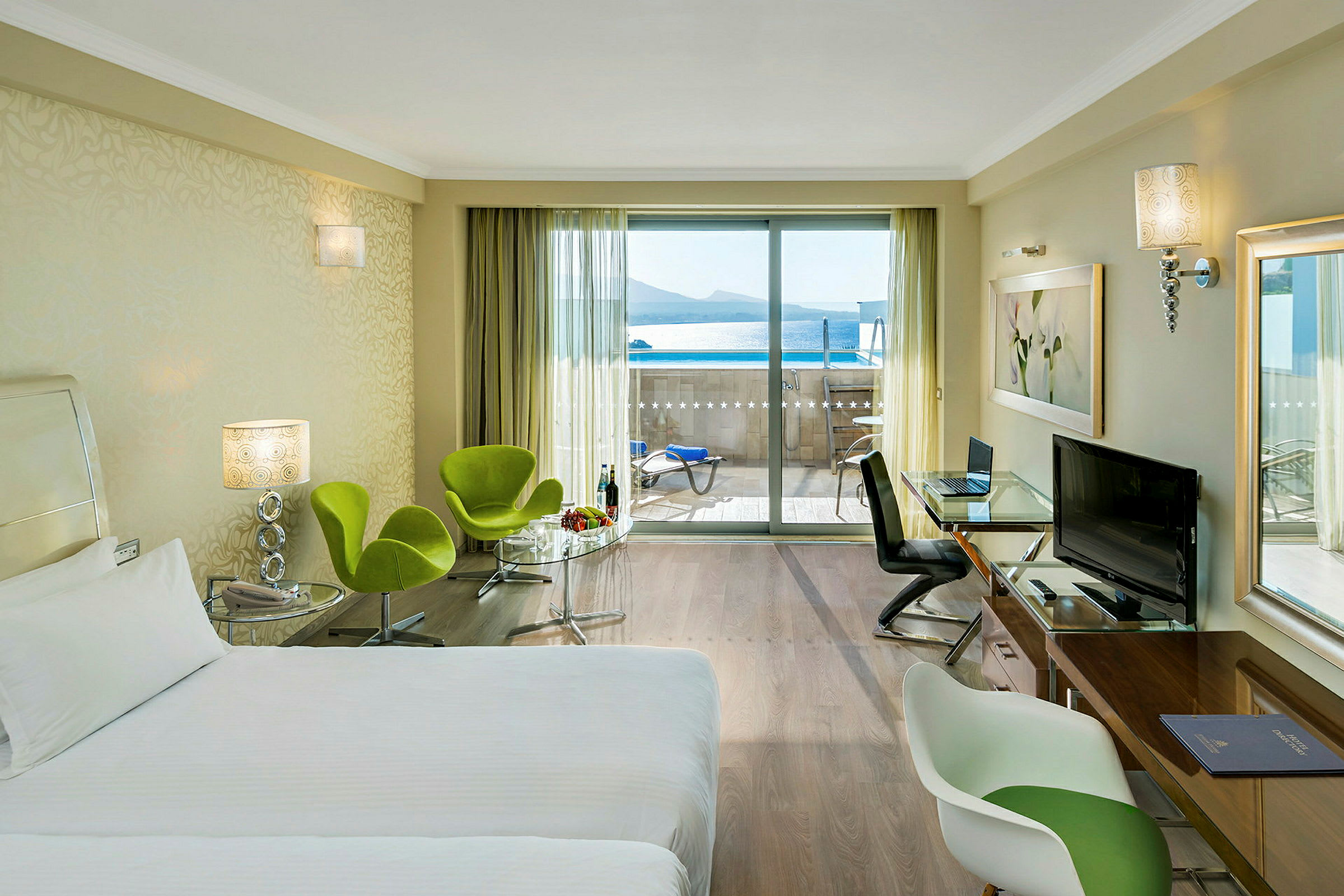 Et hotelværelse med en seng, siddepladser og et bord samt udsigt til en balkon med havudsigt. (AI-genereret tekst)