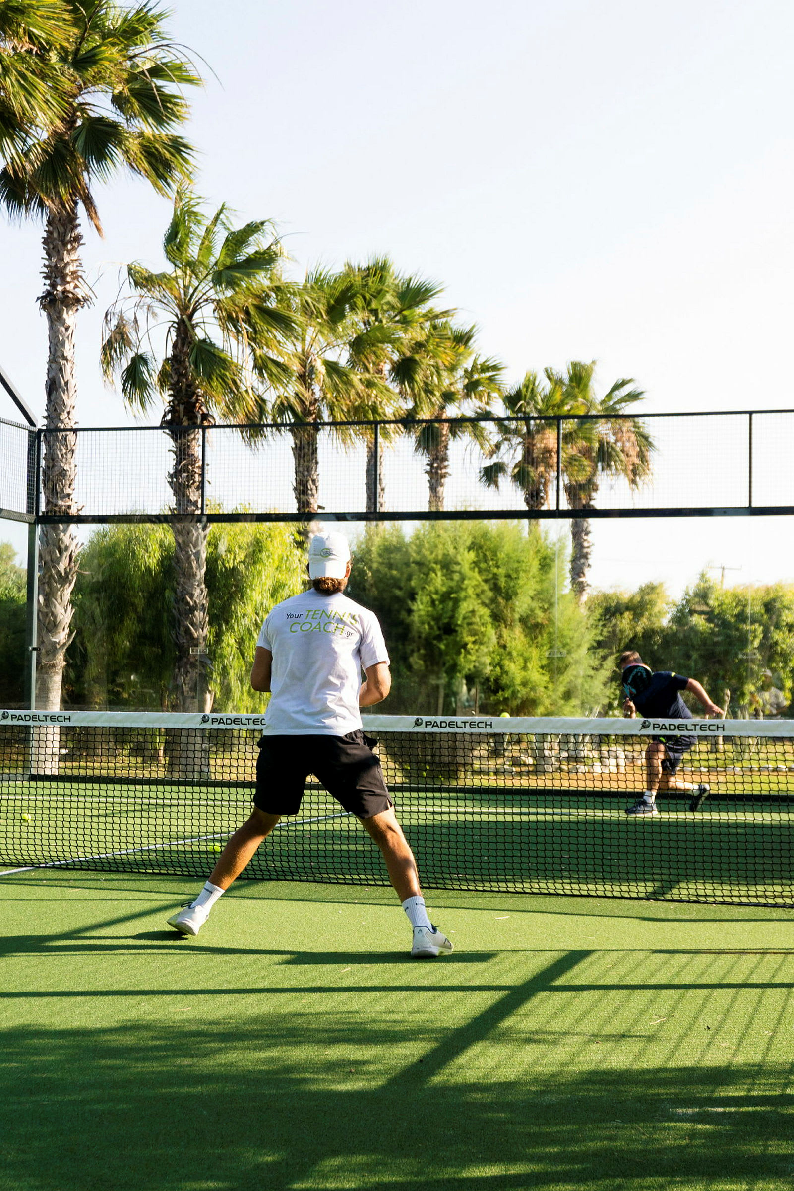 En mand spiller padeltennis på en udendørsbane med palmer omkring. (AI-genereret tekst)