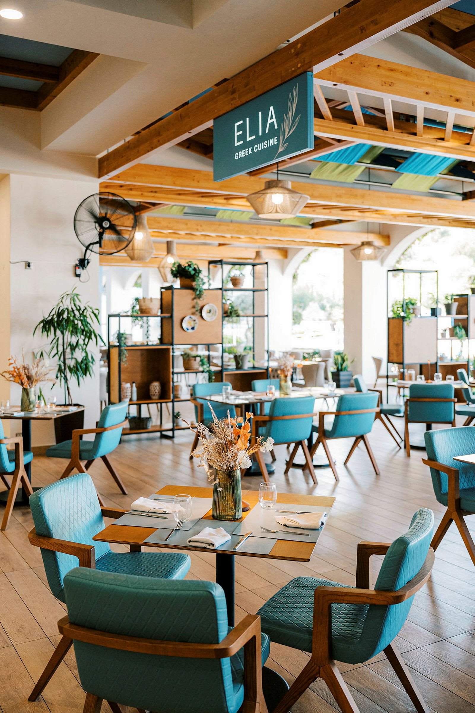 En lys og moderne restaurant med trædetaljer og blå stole. Udsmykket med planter og tørrede blomsterarrangementer. (AI-genereret tekst)