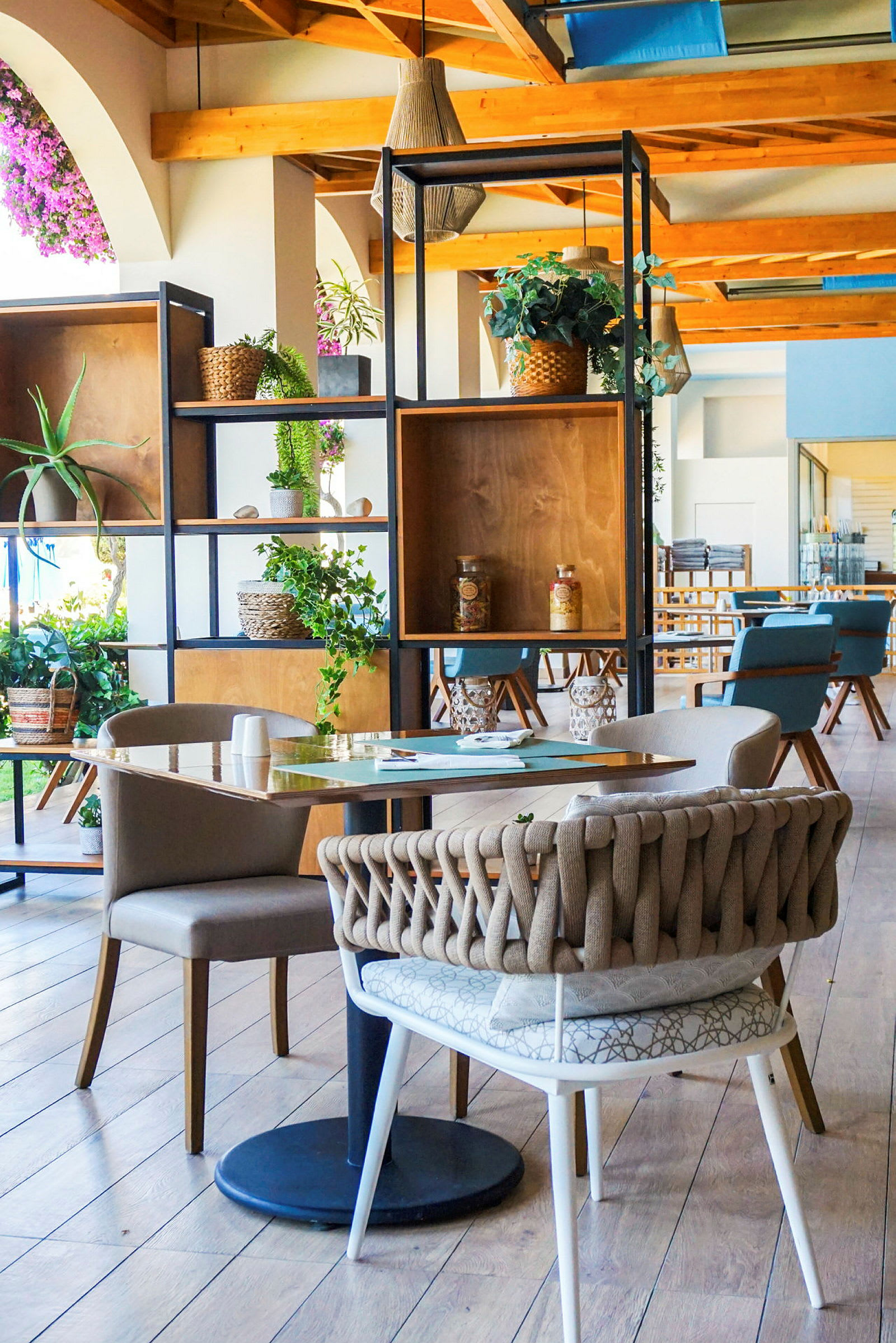 Billede af en elegant indrettet café eller restaurant med moderne møbler, trædetaljer og dekorationer med grønne planter. (AI-genereret tekst)