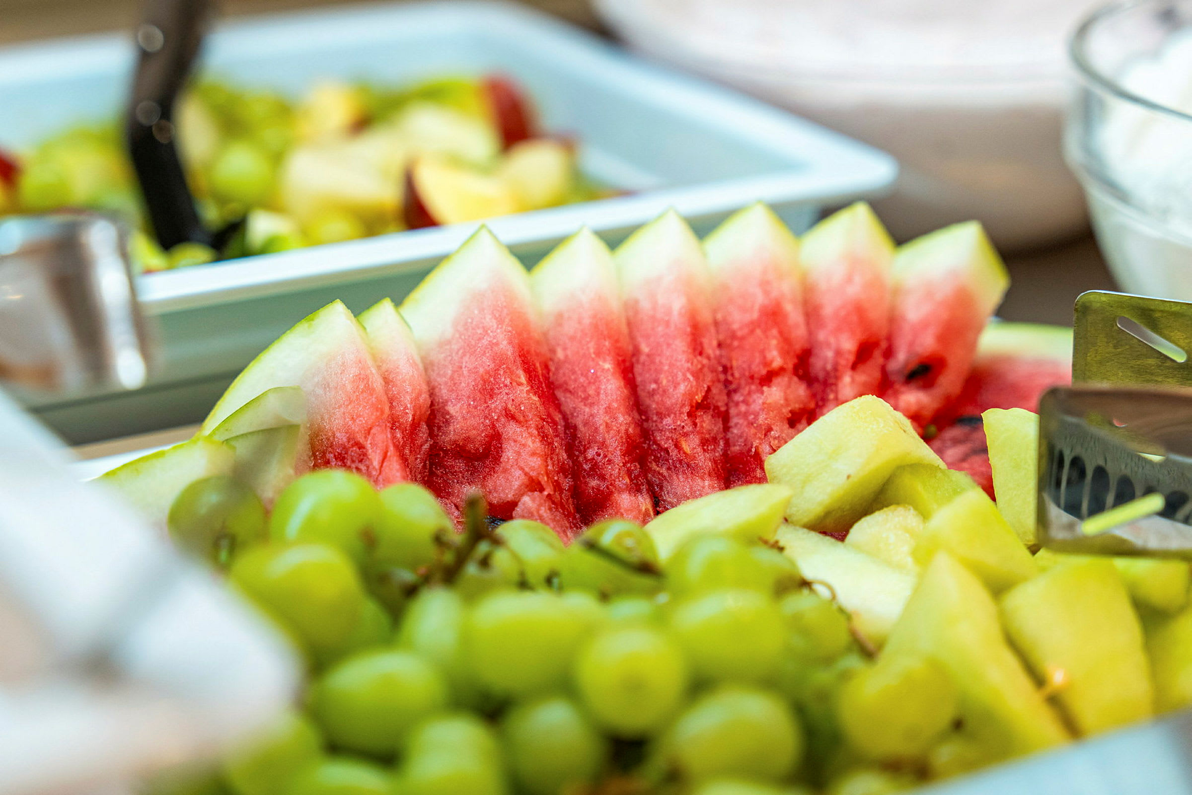 Stykker af frisk vandmelon, druer og ananas er arrangeret på et serveringsfad. (AI-genereret tekst)
